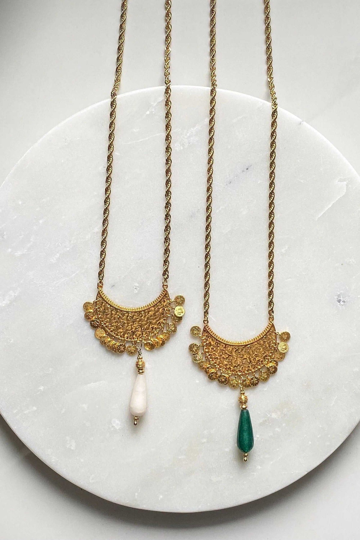 KIVÉLI Boho Necklace with two gold-toned textured pendants, ornate detailing, and white and green gemstone drops