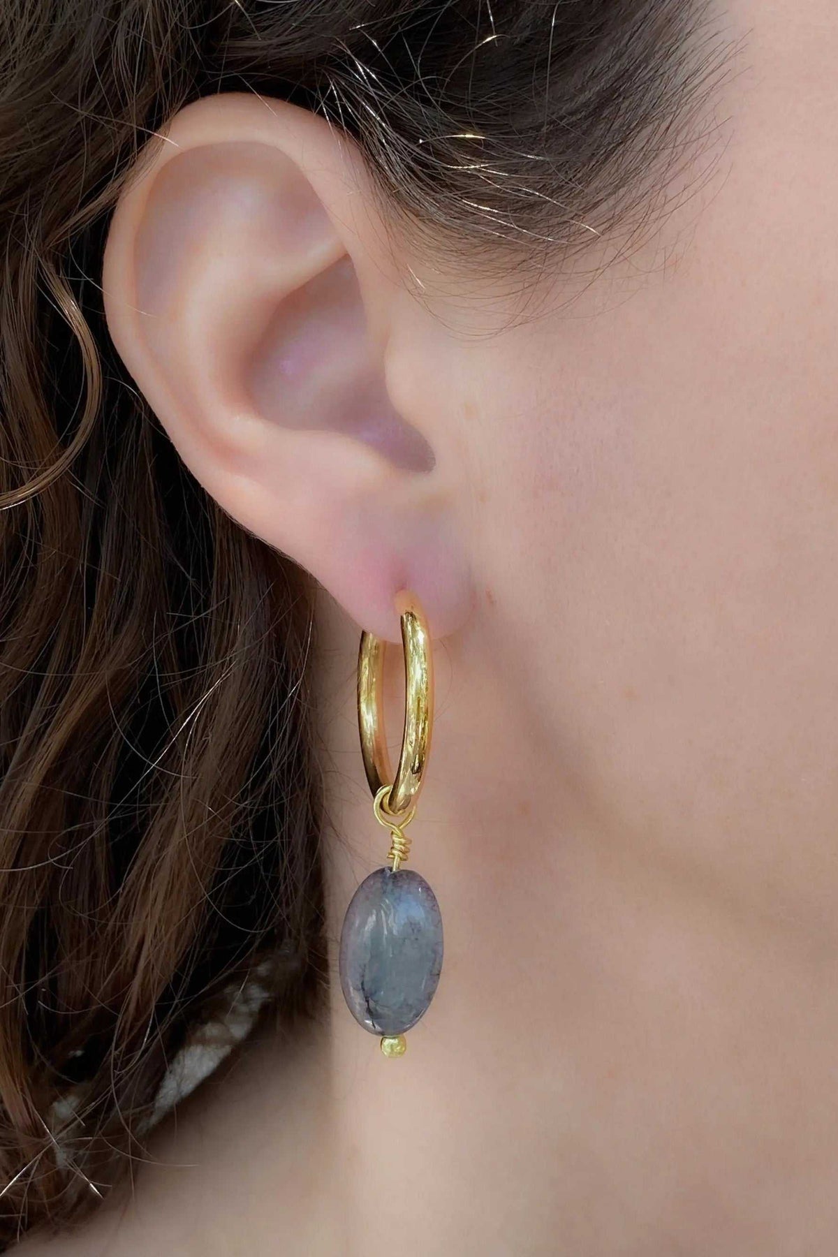 Large hoop earrings in gold-toned metal with a textured finish and dangling oval blue-grey stone charm
