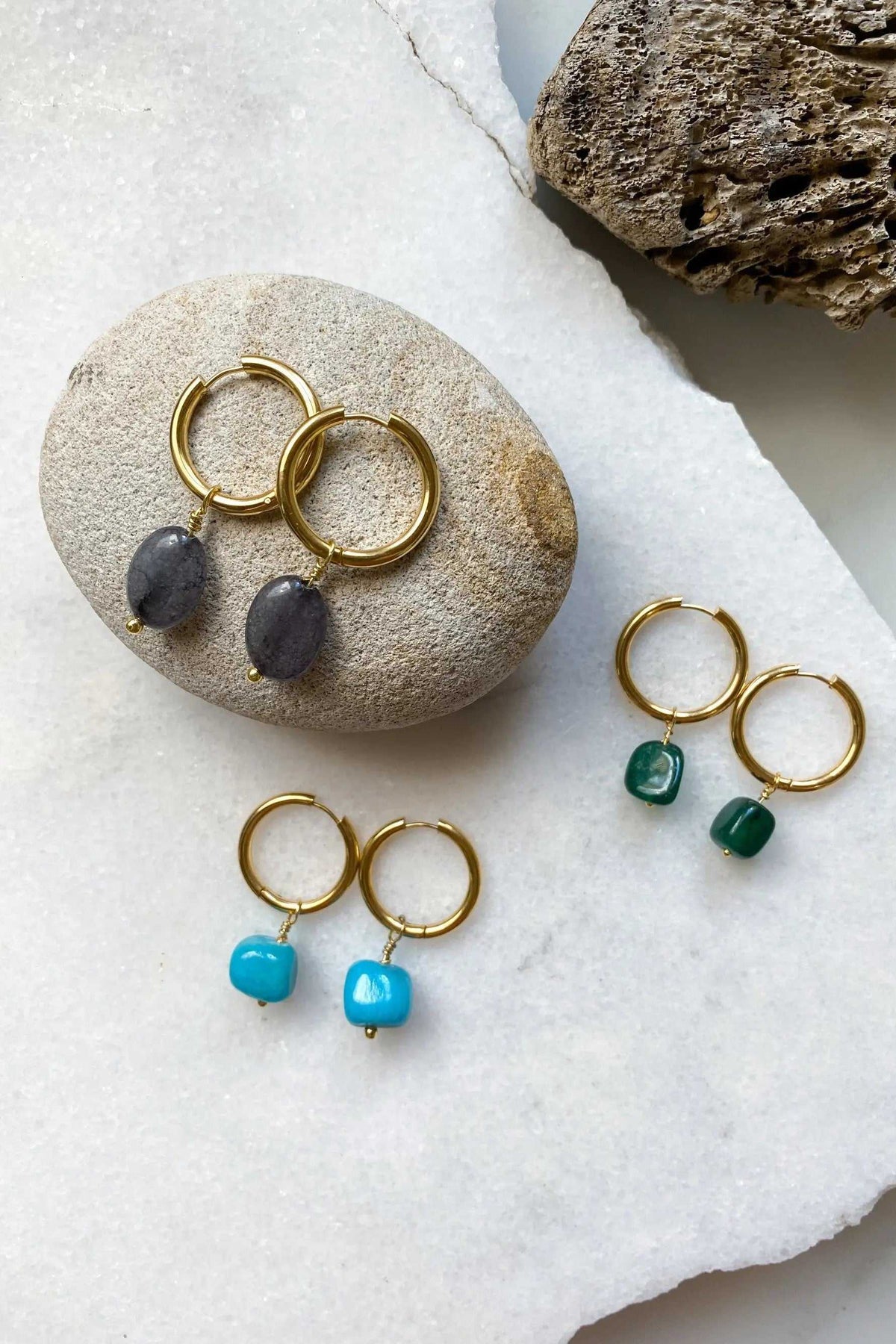 Large hoop earrings in gold-tone metal with dangling dark gray, deep green, and turquoise stone charms
