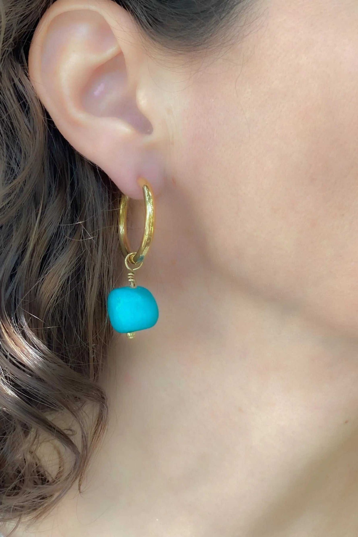 Large hoop earrings in gold-tone metal with a turquoise blue polished stone charm and textured hoop
