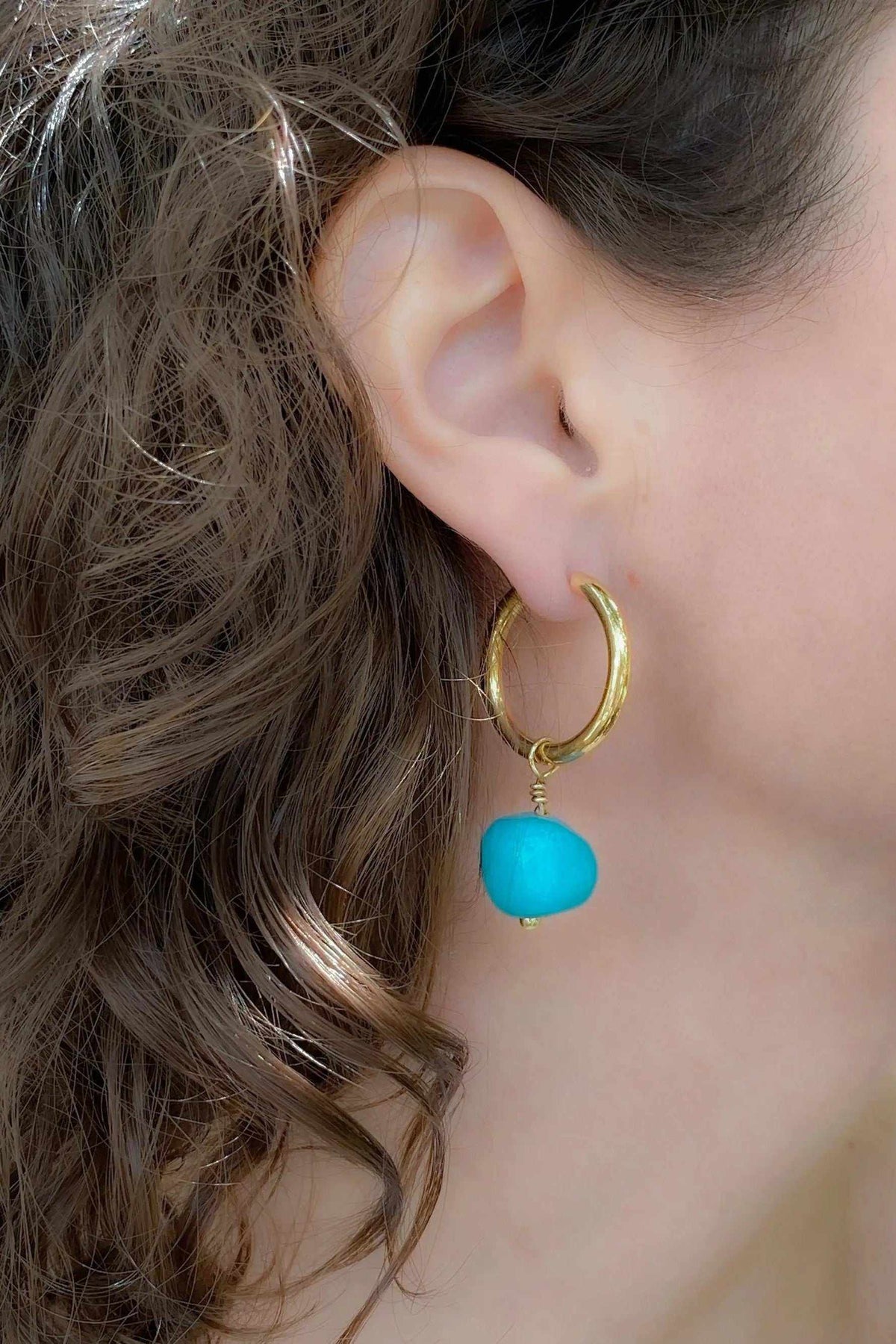 Large hoop earrings in gold-plated metal with a turquoise blue stone charm and smooth polished finish