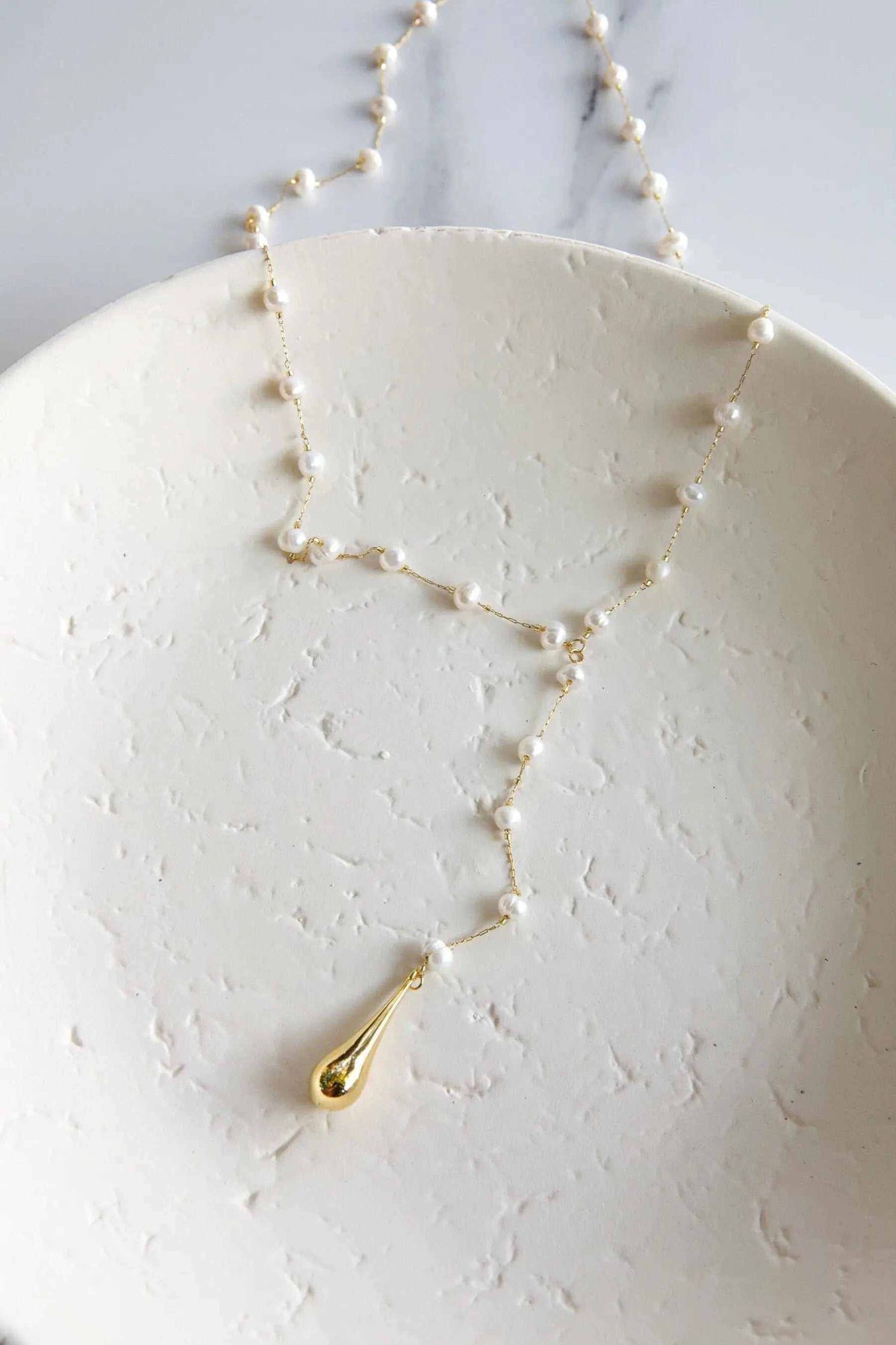 Lariat pearl necklace with delicate gold chain, white pearls, and a teardrop pendant in a long Y design
