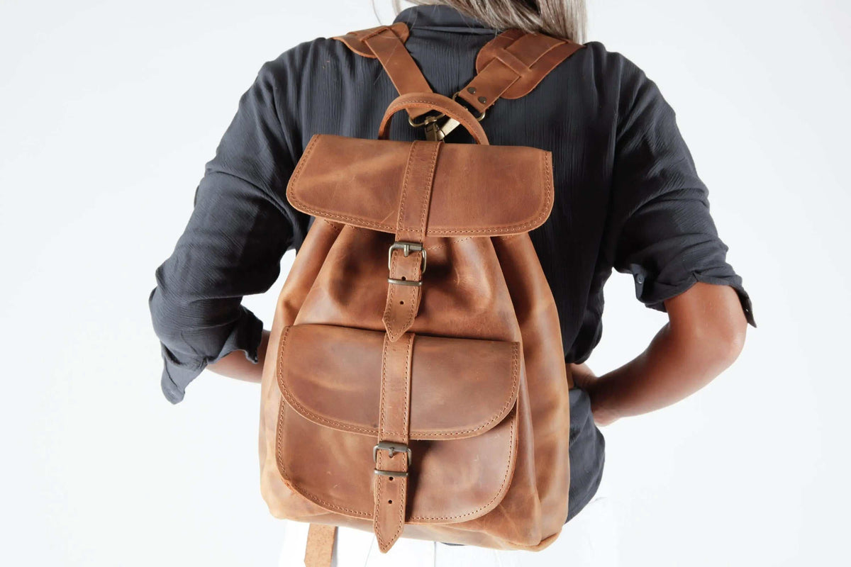 Leather backpack in warm brown leather with adjustable straps, two flap pockets, central buckled straps and a top handle
