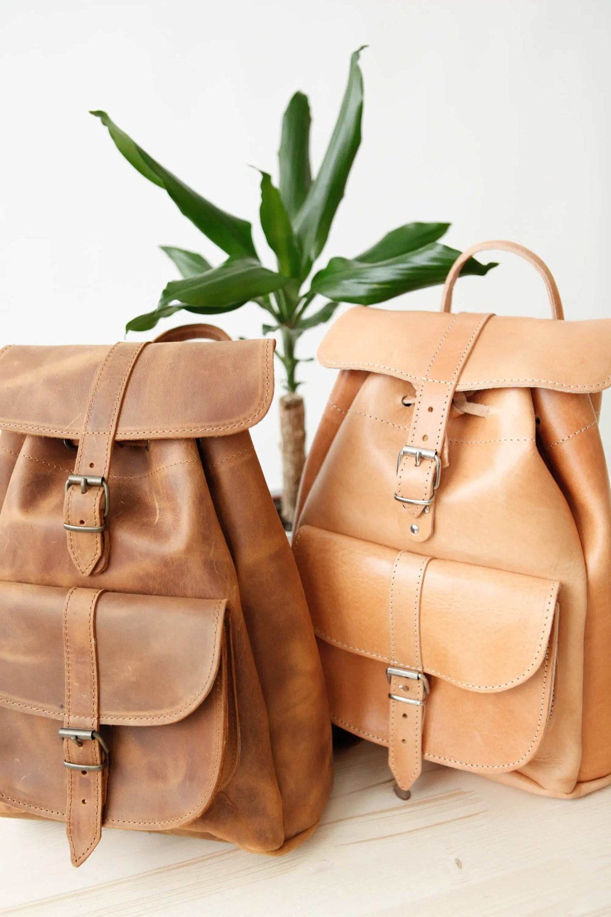Leather backpack pair in warm brown and natural tan leather, with drawstring tops, front flap pockets and metal buckles
