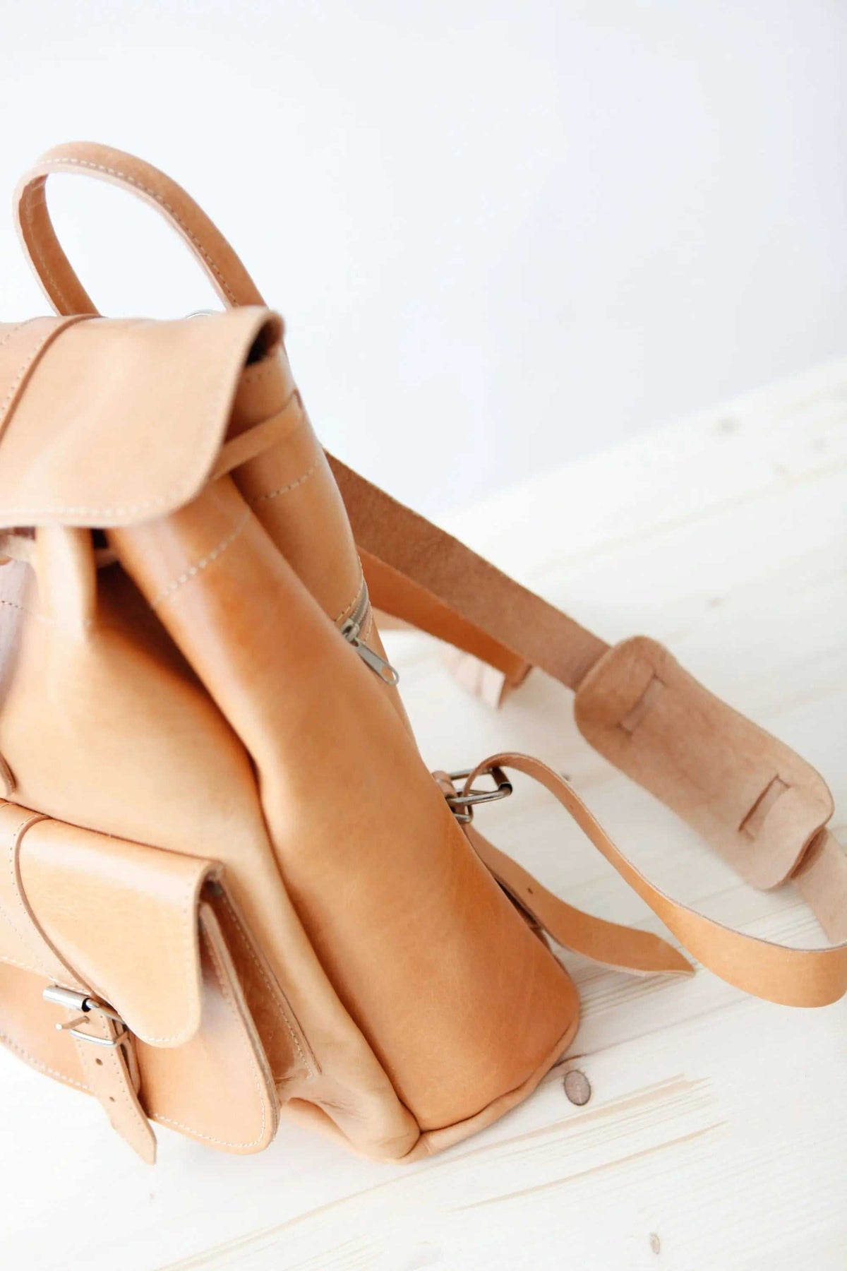 leather backpack in natural tan leather with a soft drawstring body, flap pockets, top handle and adjustable straps