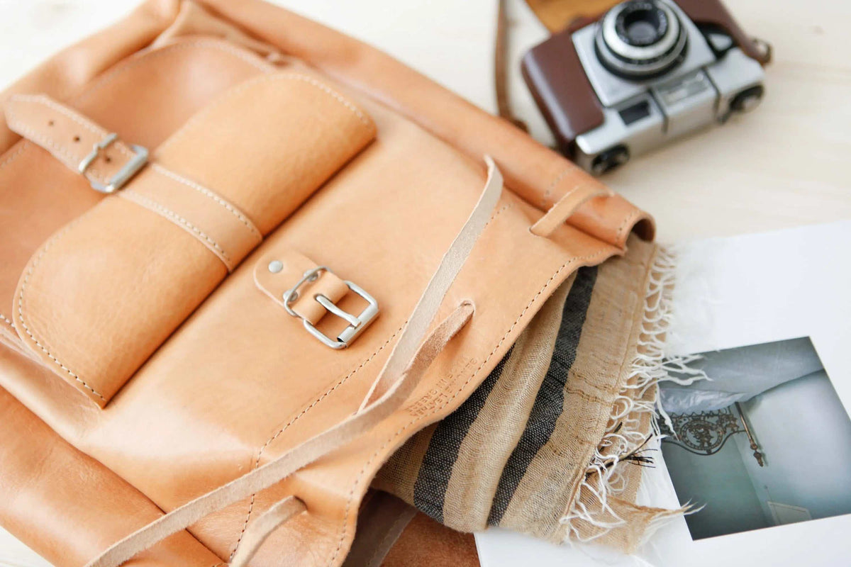 Leather backpack in natural tan leather with stitched panels, front pockets, metal buckles and a drawstring closure