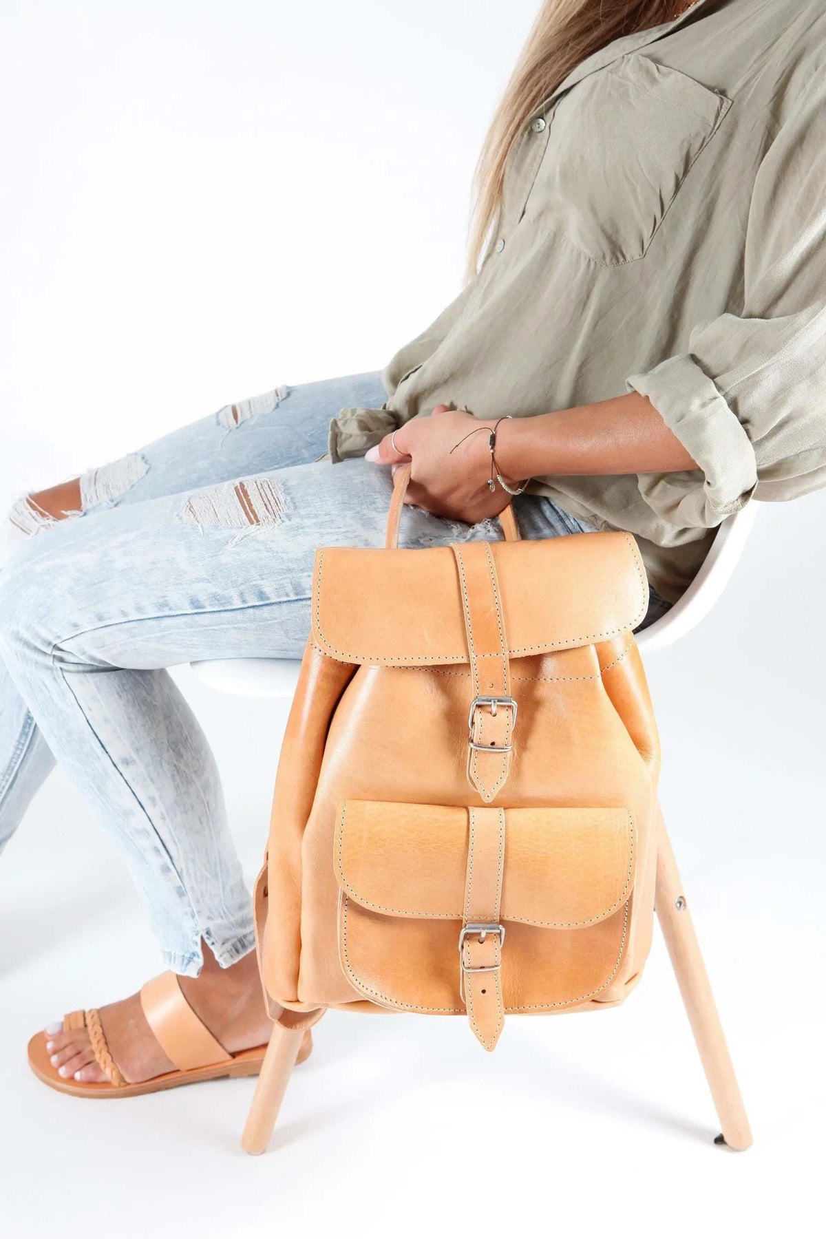 Leather backpack in warm tan leather with a structured shape, two buckle-fastened front pockets, and a top flap