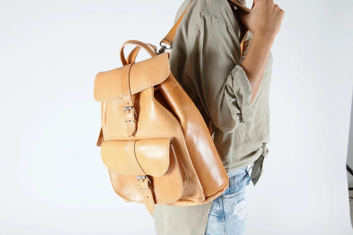 leather backpack in warm tan leather with two front flap pockets, buckle closures, drawstring top and adjustable straps