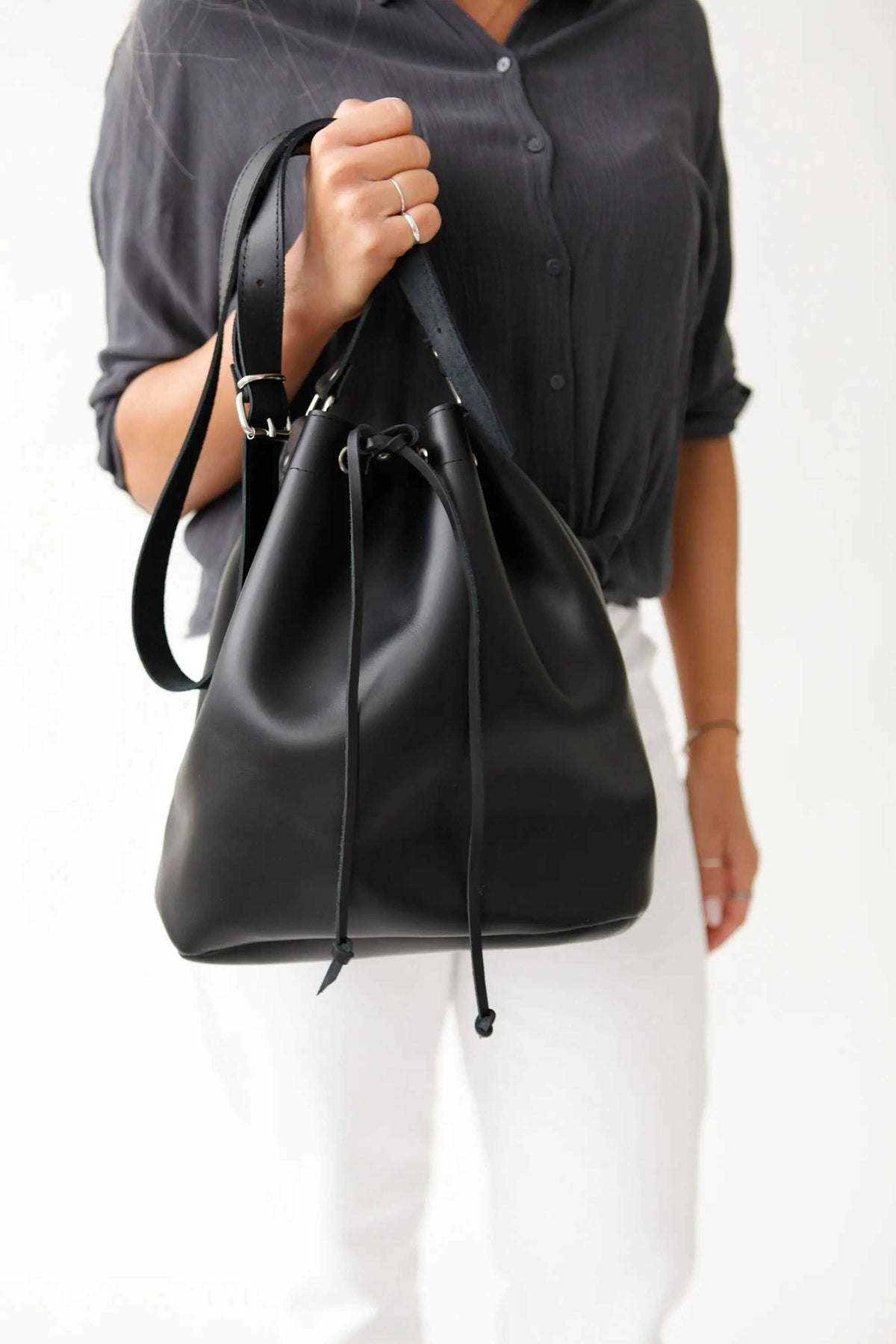 leather women's handbag in black with a smooth finish, bucket shape, adjustable strap, drawstring closure and metal buckles