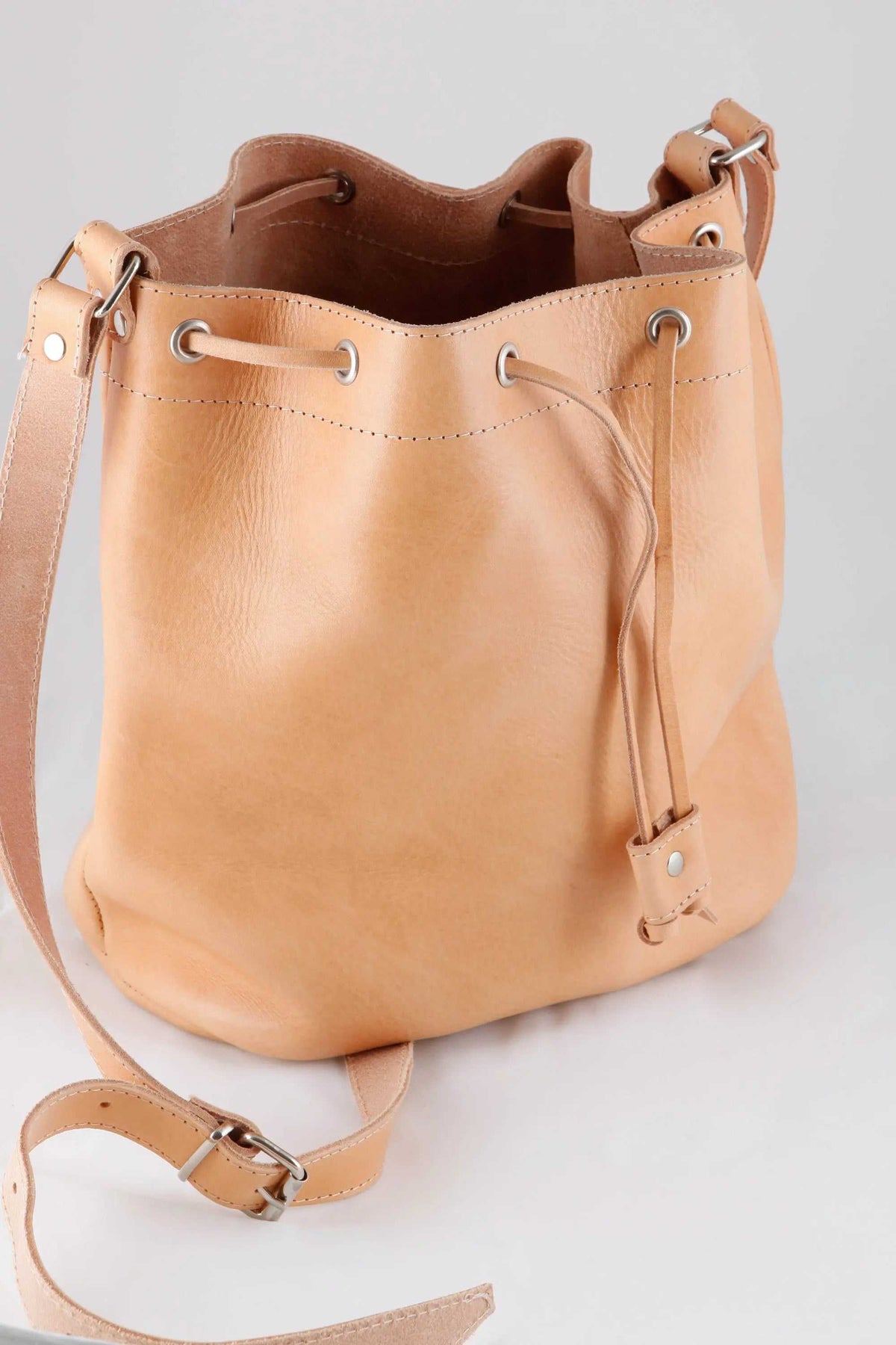 leather women's handbag in light tan leather, with a bucket shape, drawstring closure and adjustable shoulder strap