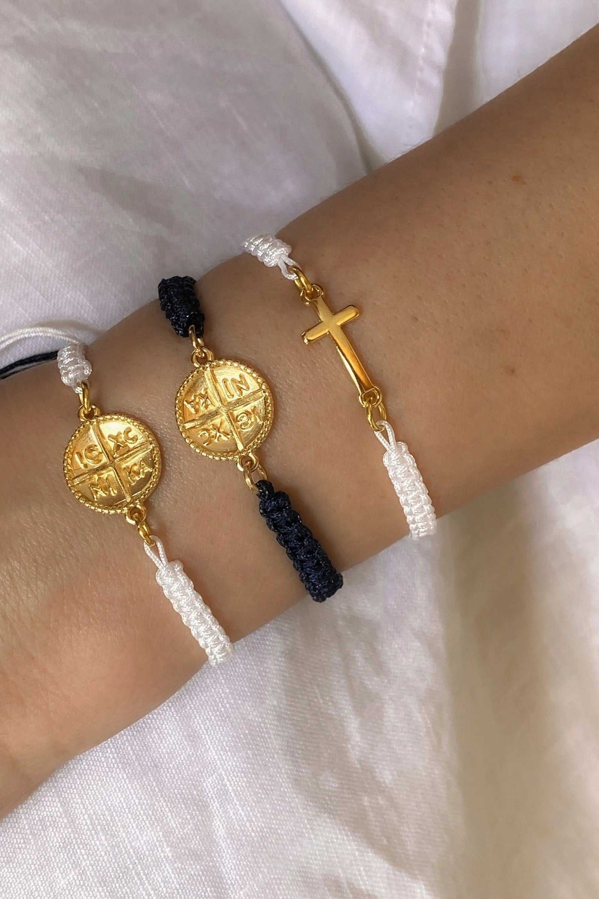 Macrame braided Bracelet in white and dark blue cord, featuring gold Byzantine coin motifs and a cross charm