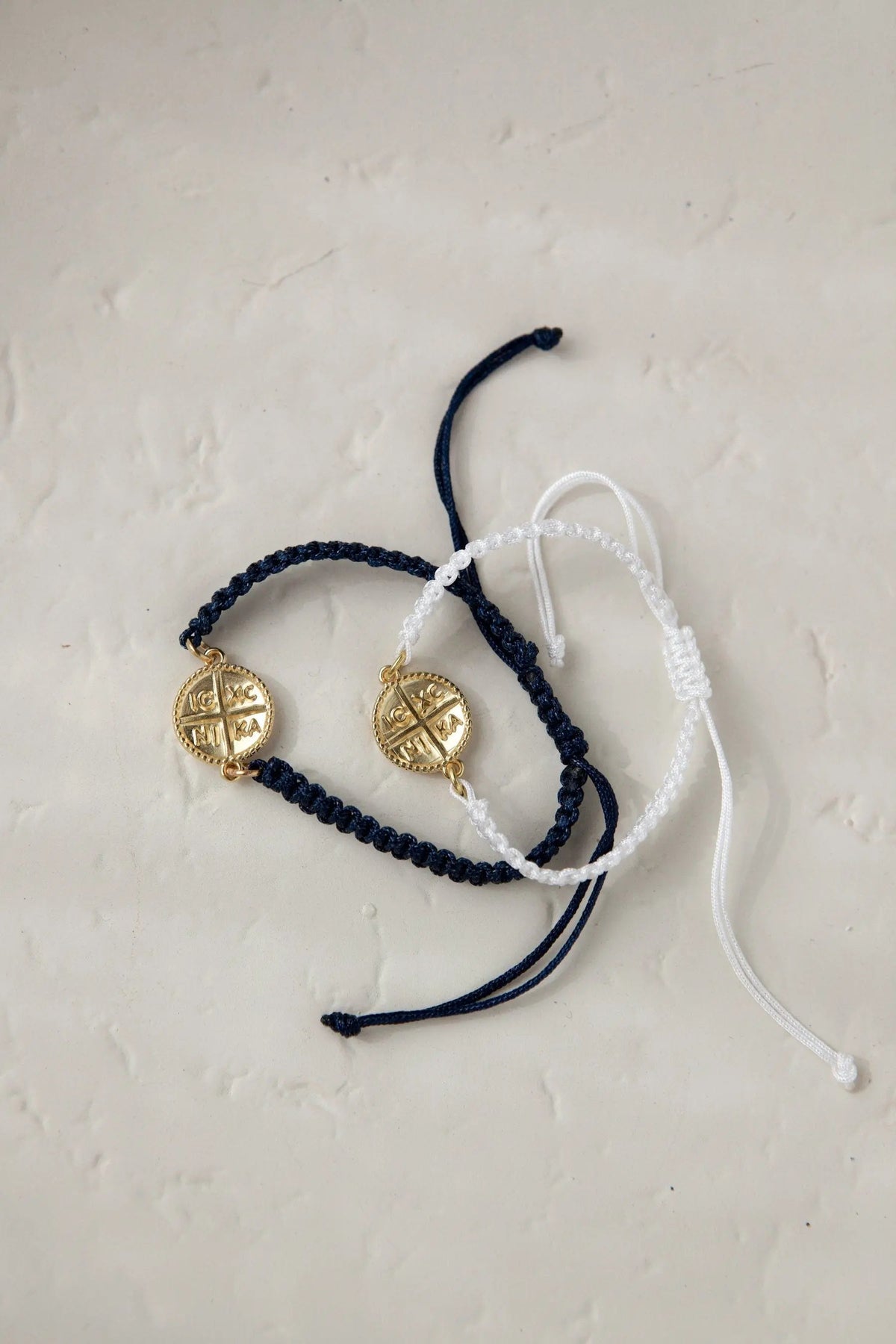Macrame cross bracelet in dark blue and white braided cord, each with a round gold-tone cross charm and adjustable sliding ties