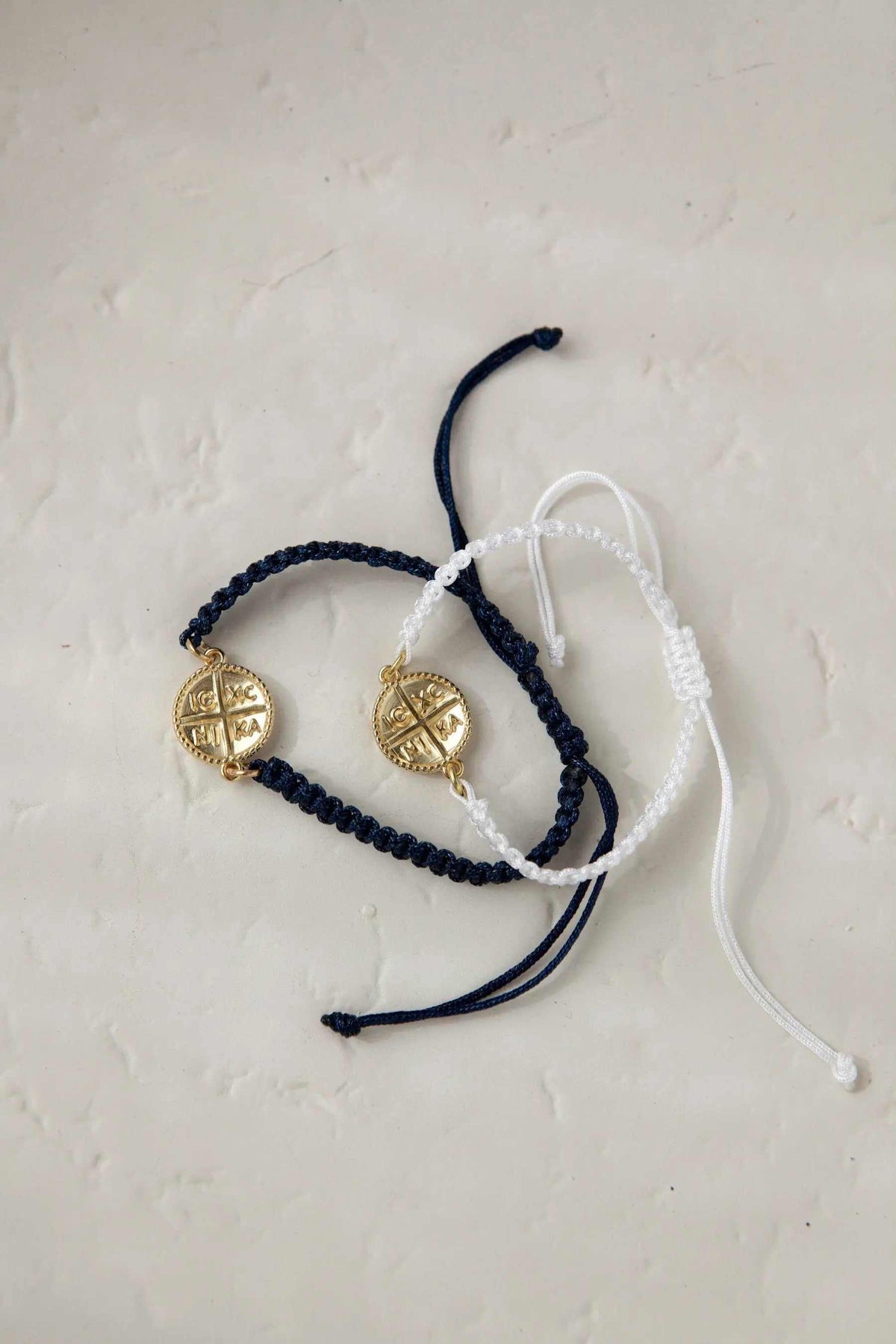 Macrame cross bracelet in dark blue and white woven cord with round gold-tone Byzantine cross charms and adjustable ties