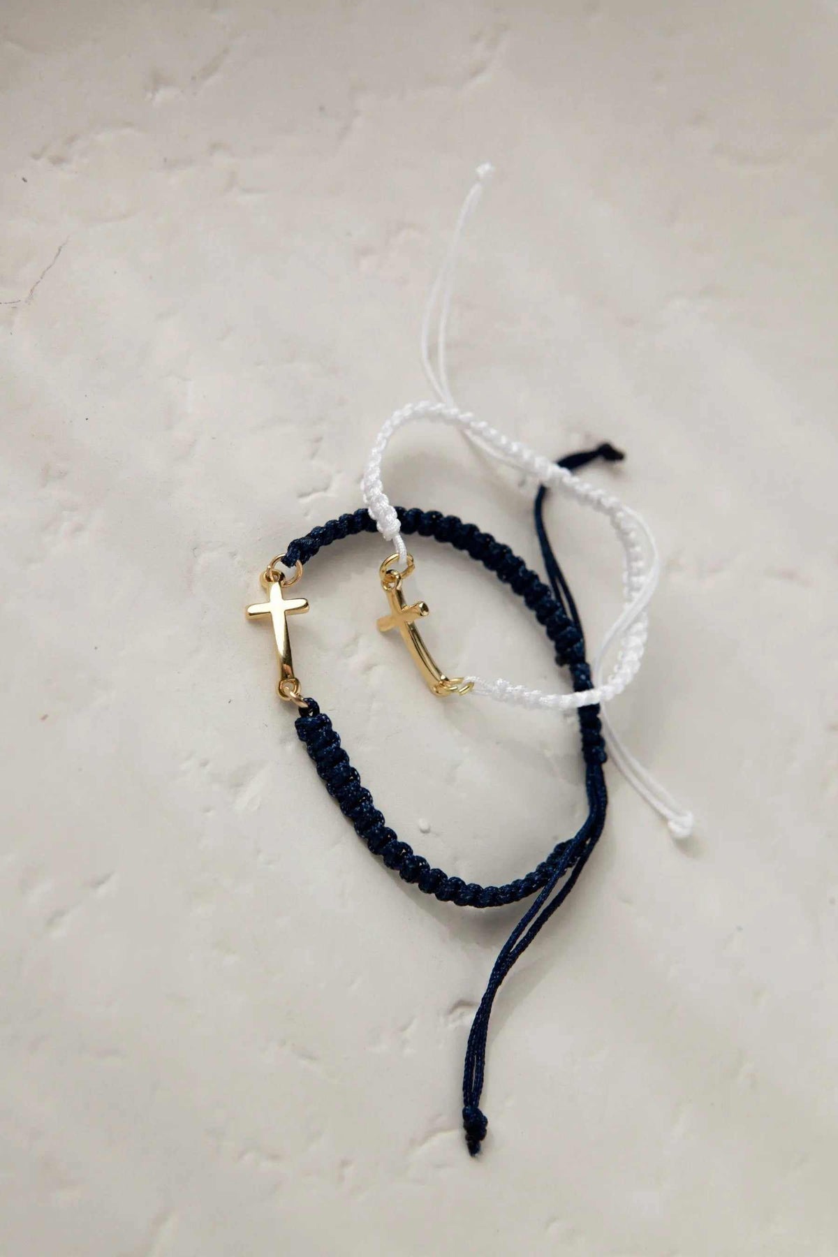 Macrame cross bracelet in dark blue and white braided cord, featuring gold-tone cross charms and adjustable ties