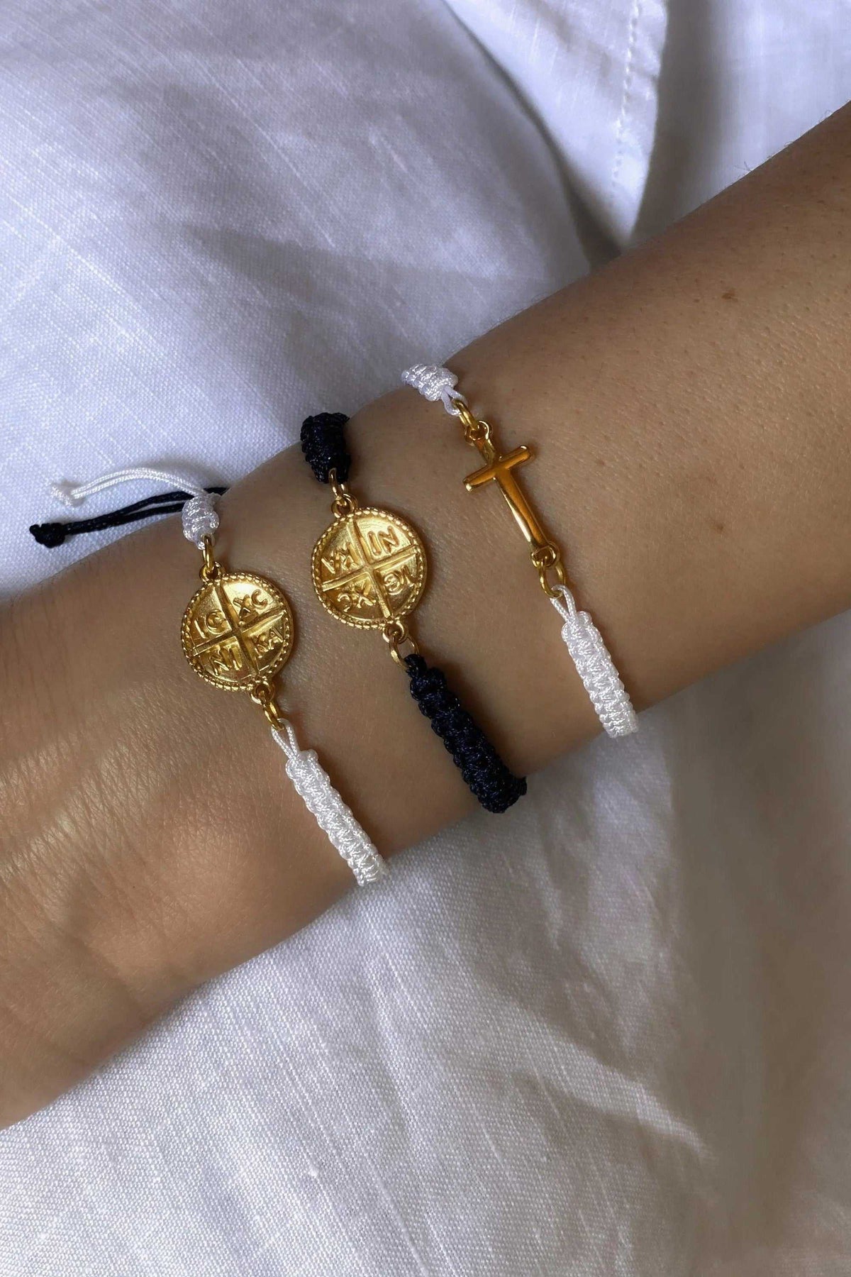 Macrame cross bracelet in white and black braided cord with gold-tone cross and Byzantine medallion charms