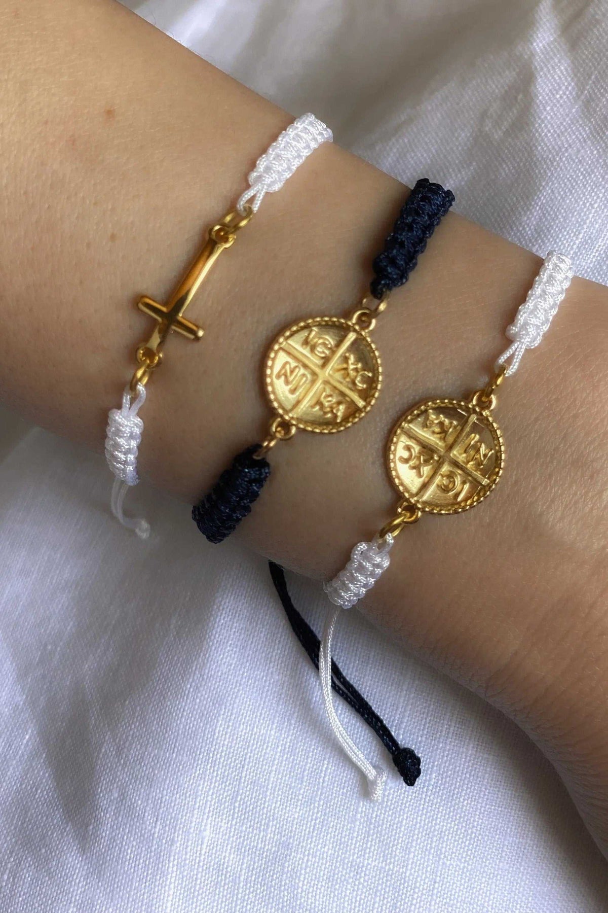 Macrame cross bracelet in white and dark blue braided cord with adjustable ties and gold-tone cross and Byzantine coin charms