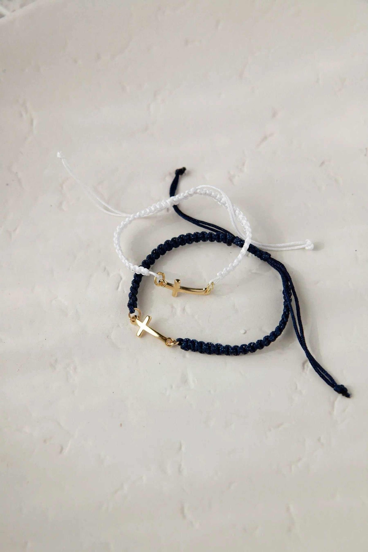 Macrame cross bracelet in white and dark blue woven cord with small gold-tone cross charms and adjustable ties
