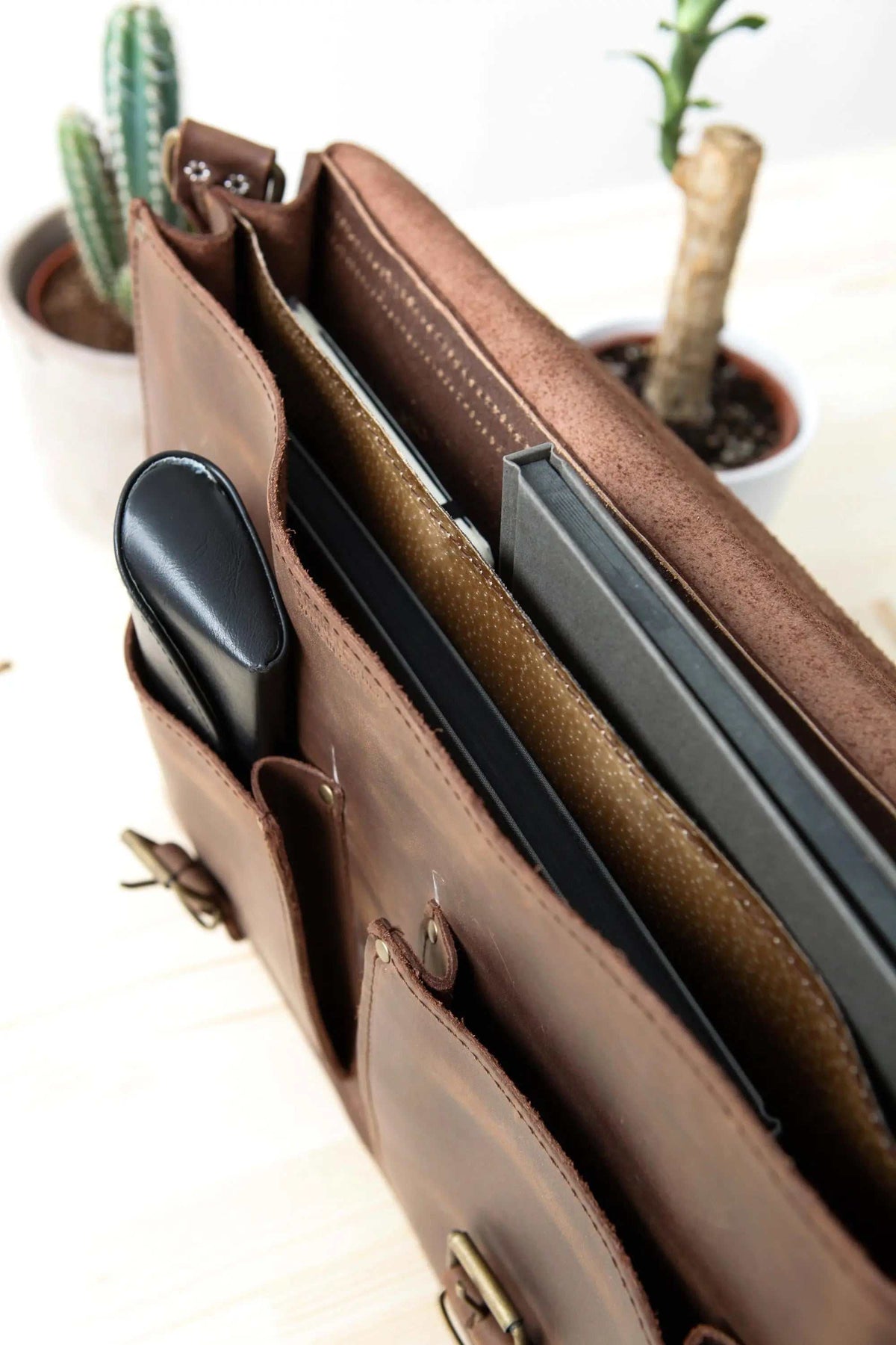 MEN'S BRIEFCASE with pocket in brown leather, showing a structured open top, front pockets and metal buckle hardware