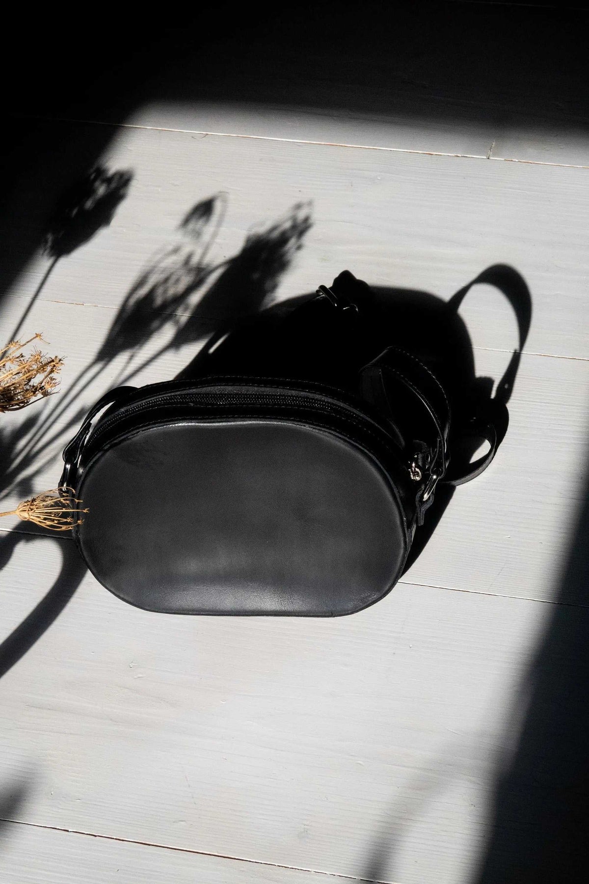 minimal shoulder bag in black leather with an oval shape, zip closure, adjustable strap and metallic buckles