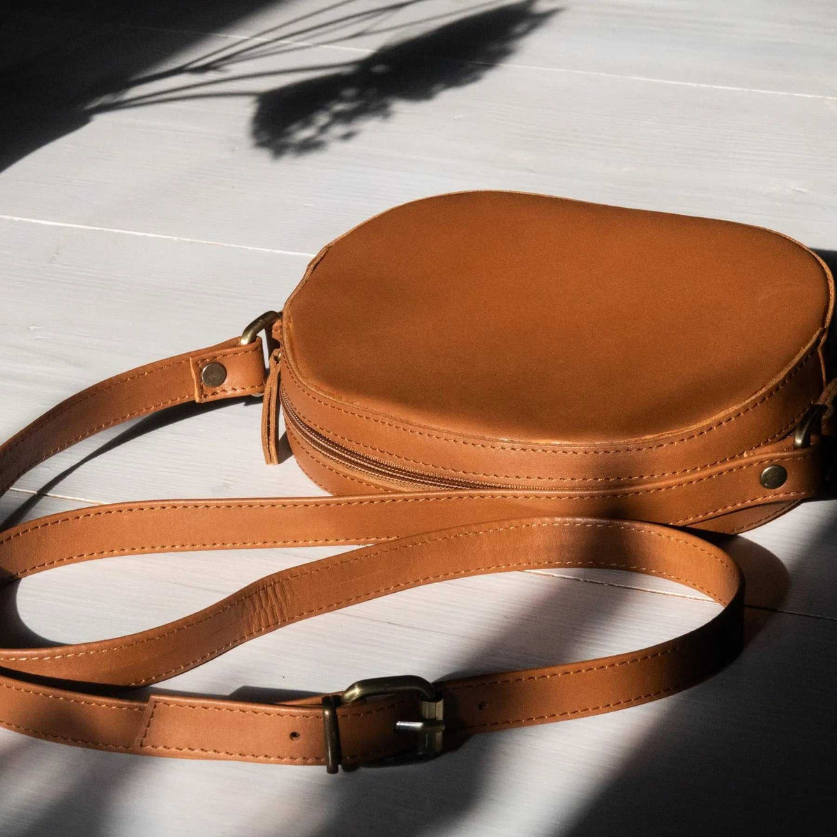 Minimal shoulder bag in warm cognac leather with an oval shape, stitched edges, zip closure and adjustable strap