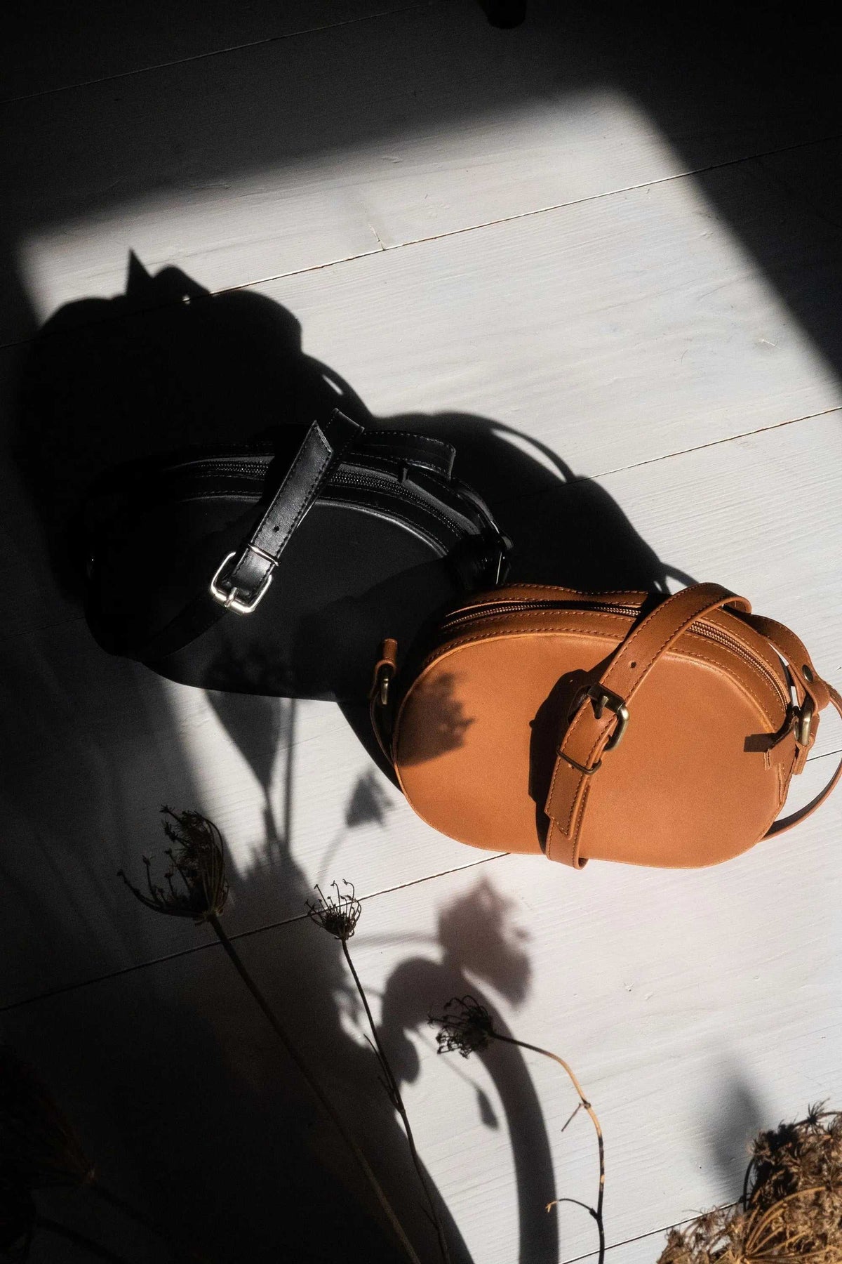 minimal shoulder bag in tan leather with an oval shape, adjustable strap, and metallic buckle details