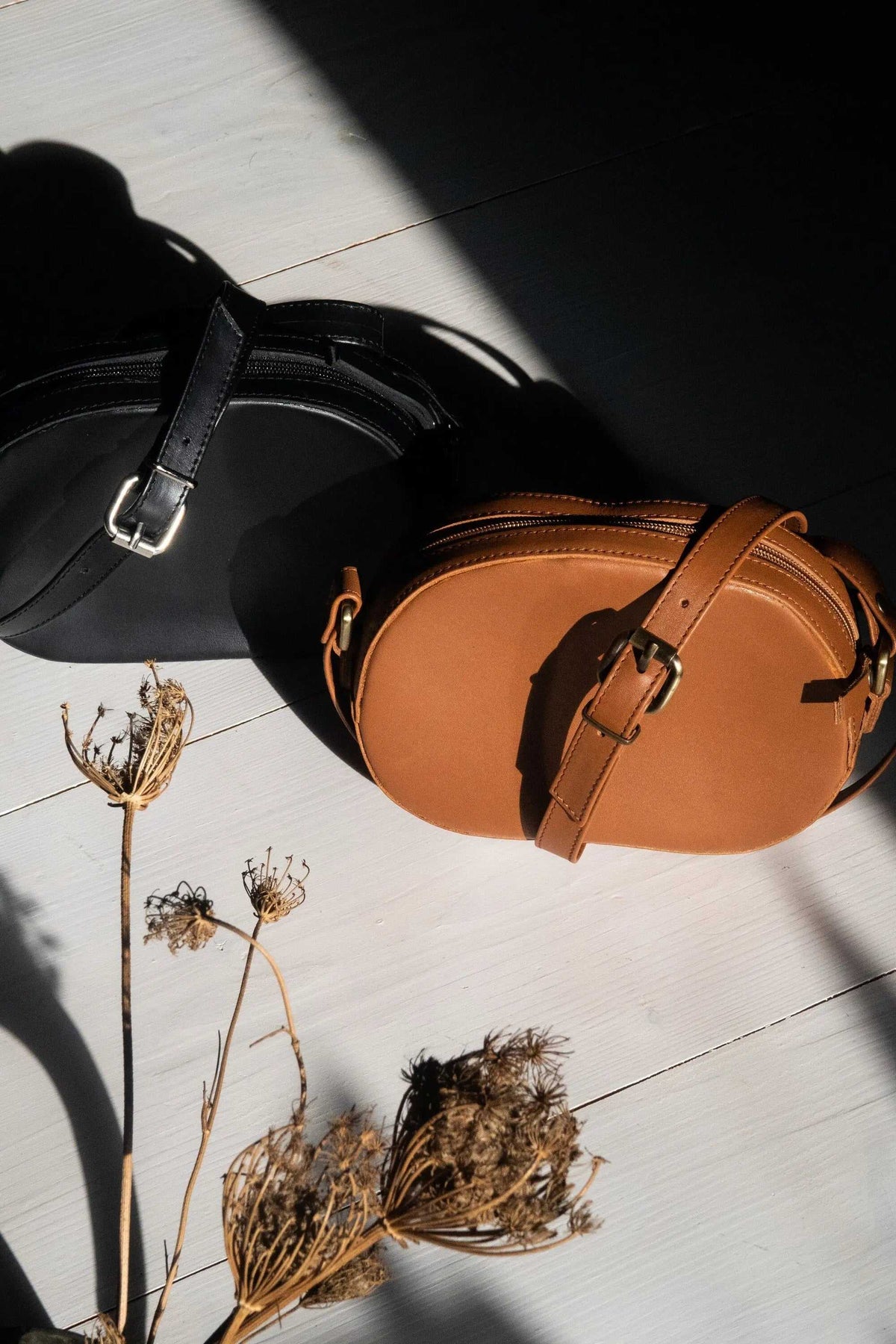 minimal shoulder bag in tan full-grain leather with an oval shape, adjustable buckle strap, and zip closure