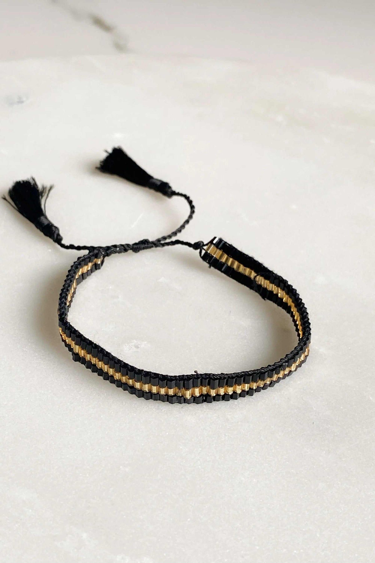 Miyuki beads bracelet with black and gold glass beads in a woven band, finished with adjustable black cord and tassels