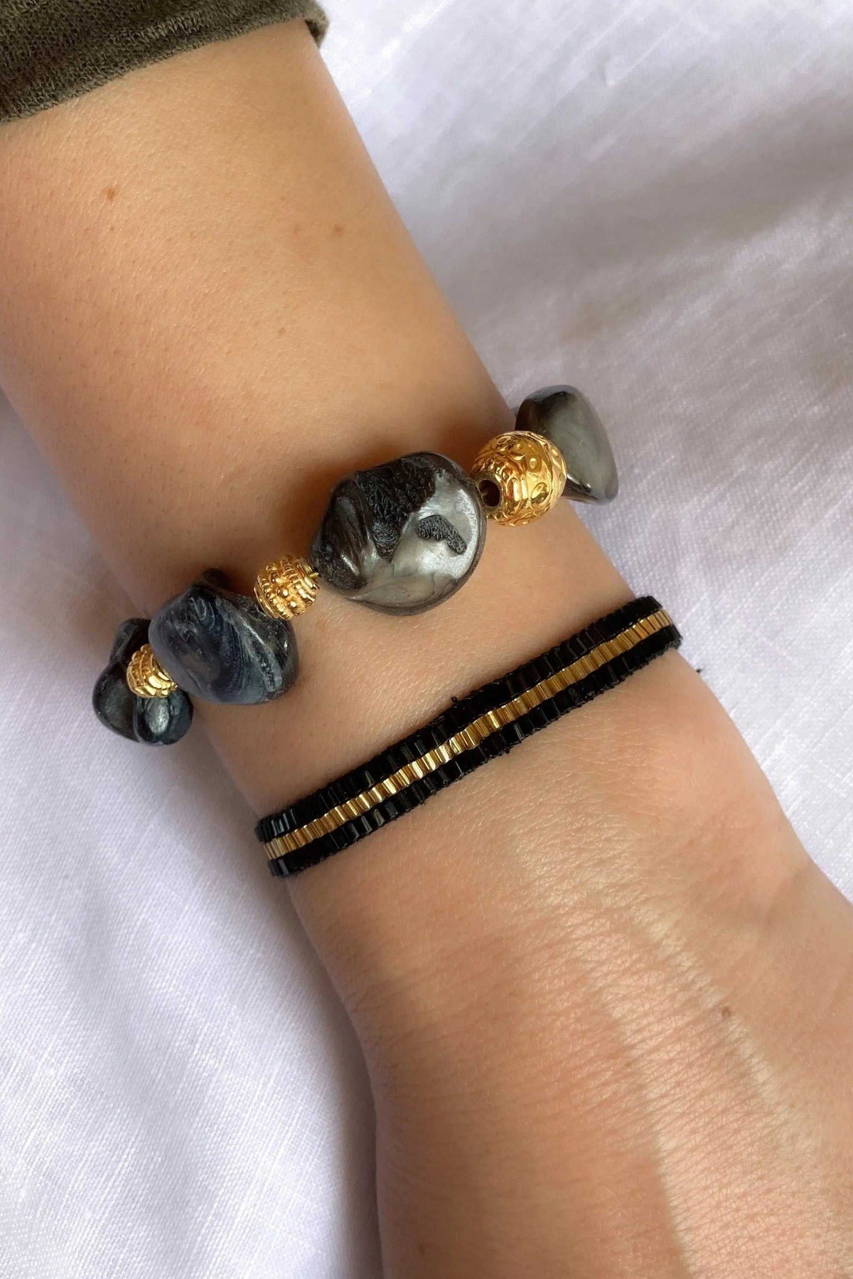 Miyuki beads bracelet set with a black woven band and a bracelet featuring glossy grey stones and gold beads