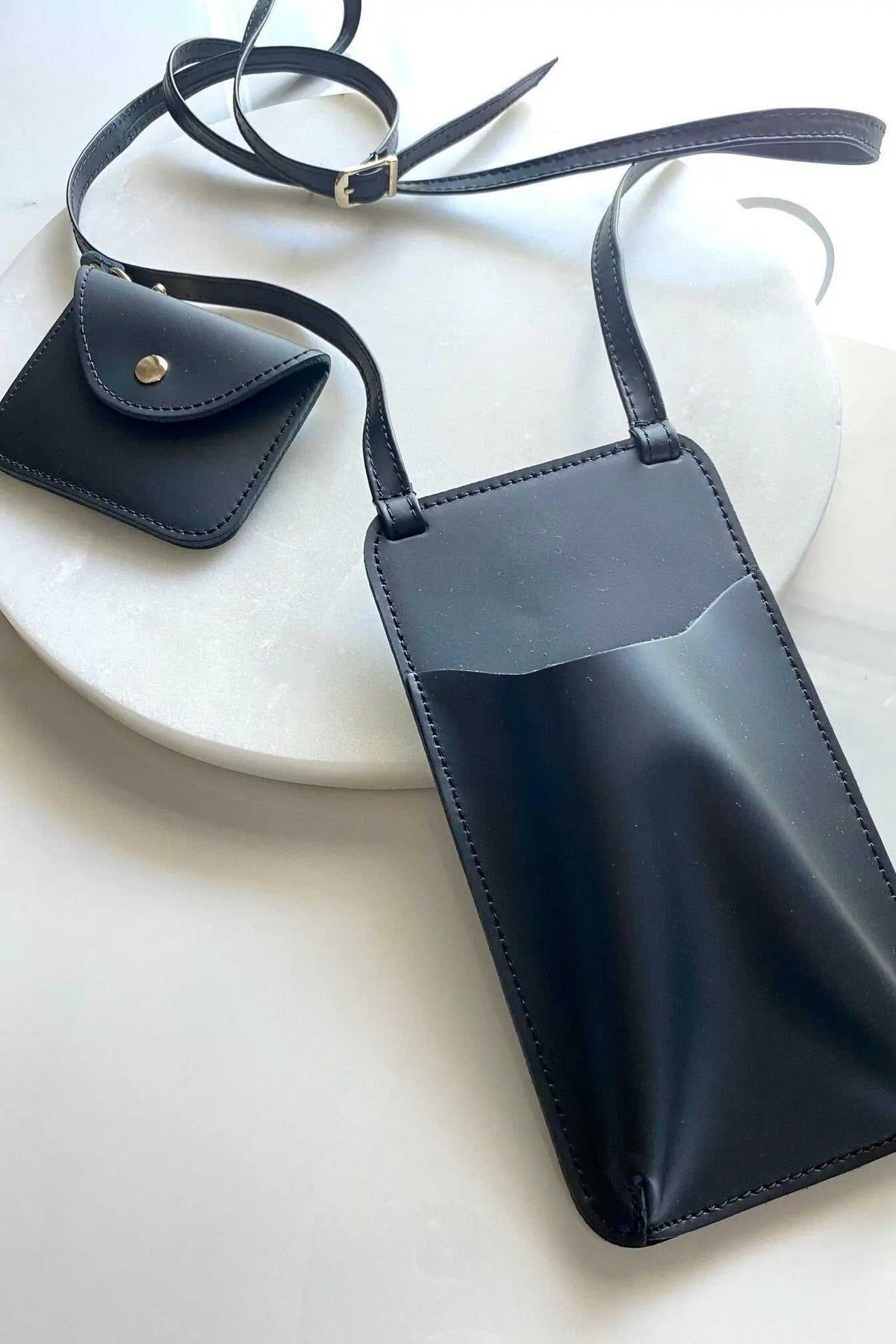 Phone Pouch in black full-grain leather with adjustable strap, metal buckle and matching snap AirPod case