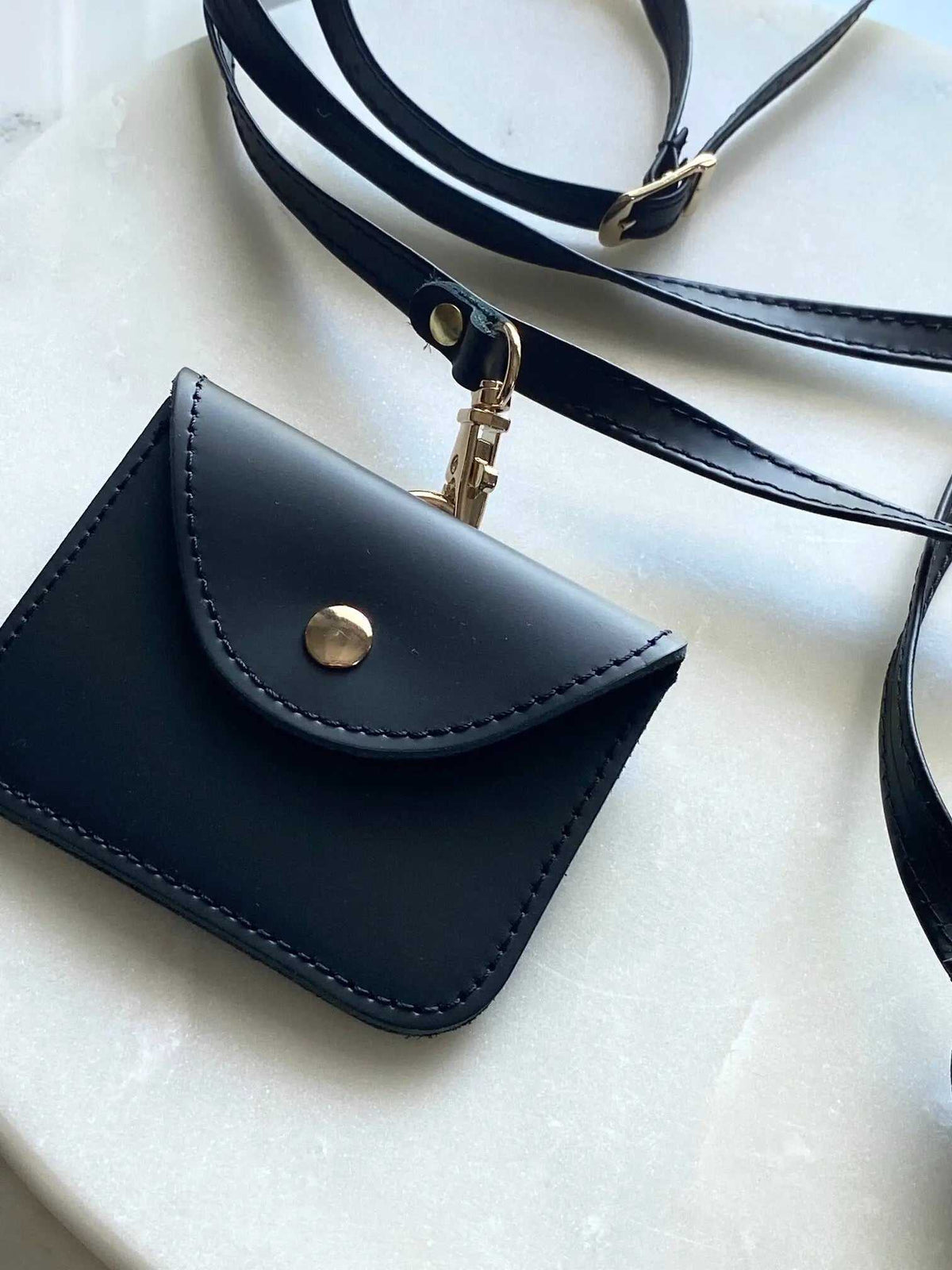 Phone Pouch in black full-grain leather with a flap, gold snap button, and adjustable shoulder strap