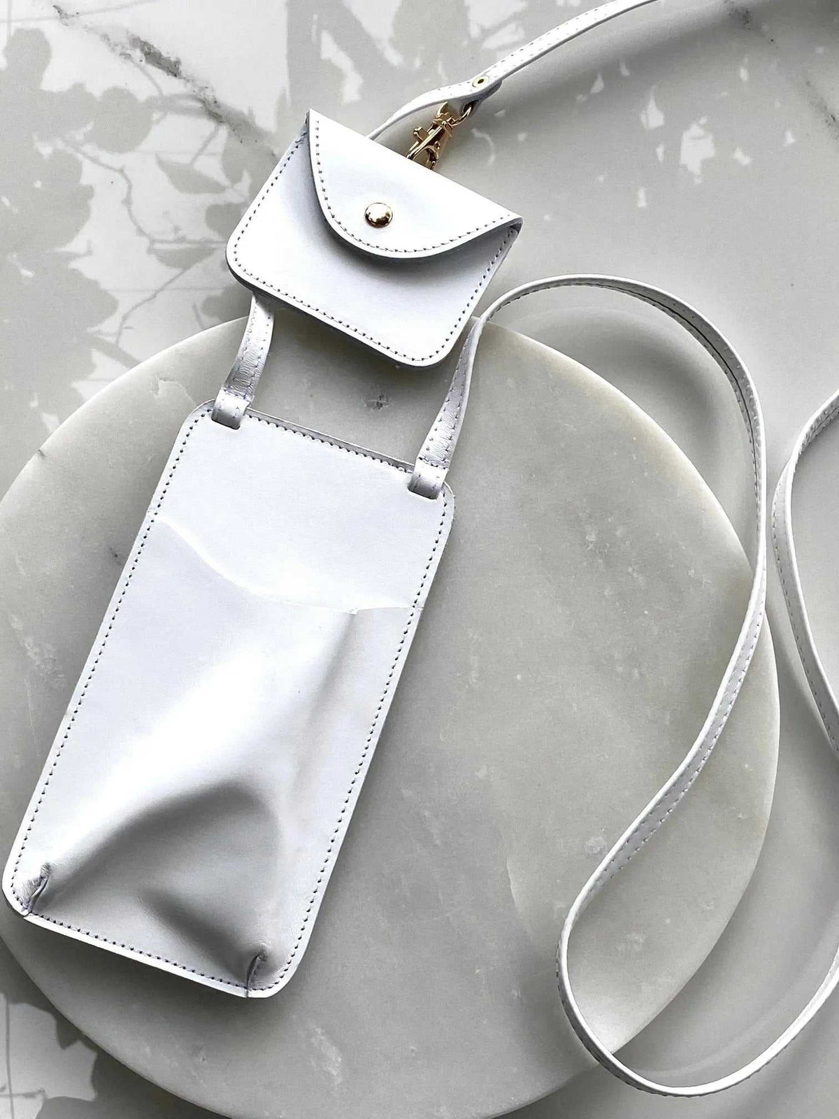 Phone Pouch in smooth white leather with a long adjustable shoulder strap, envelope flap, and gold-tone snap