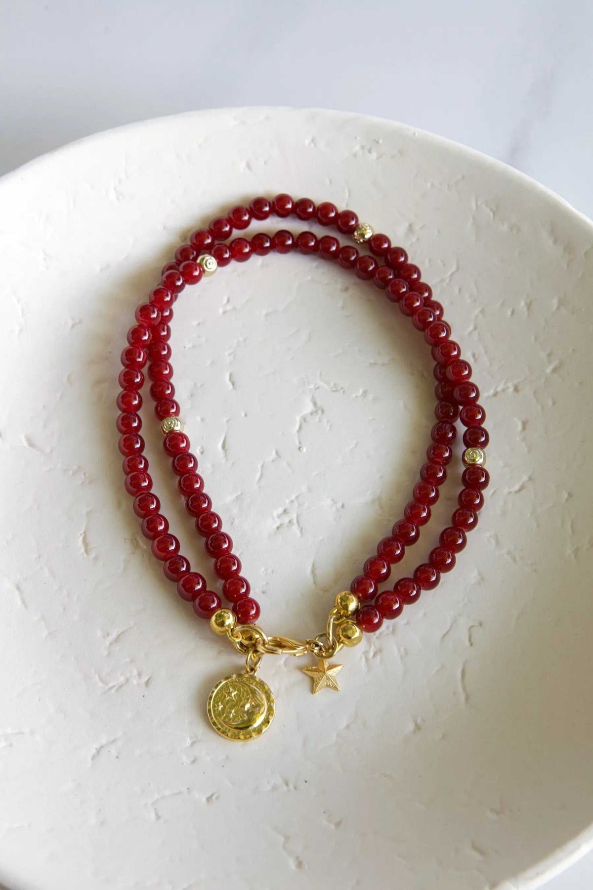 Red crystal beaded Bracelet with glossy deep red round beads, gold-tone accents, and sun medallion and star charms.