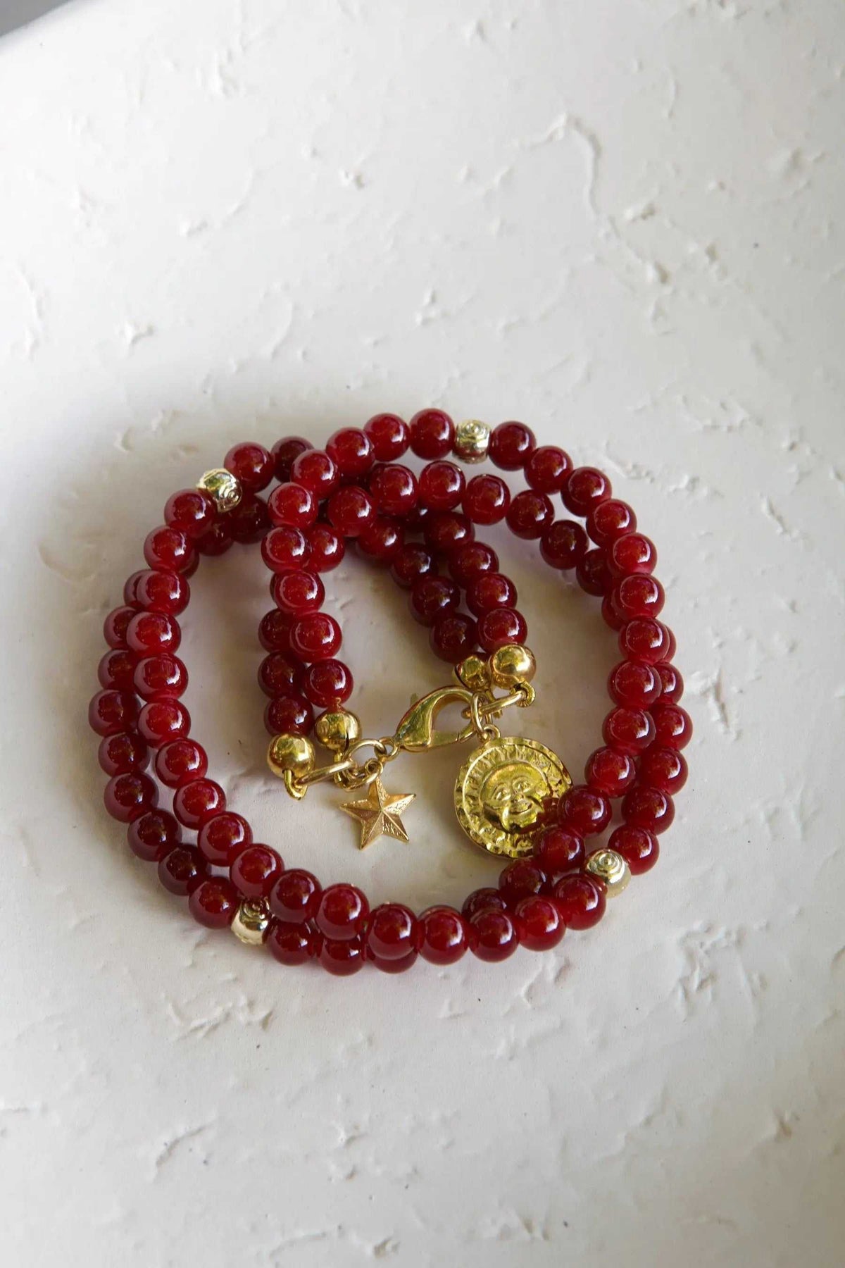 Red crystal beaded Bracelet with glossy deep red beads, small gold accents, and a sun medallion and star charms