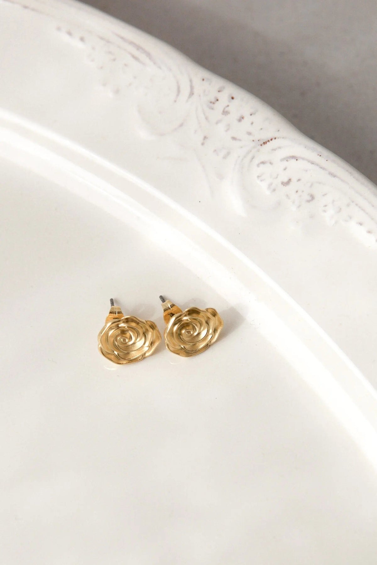 Rose earrings in gold-tone metal, shaped as small sculpted roses with layered spiral petals and straight posts