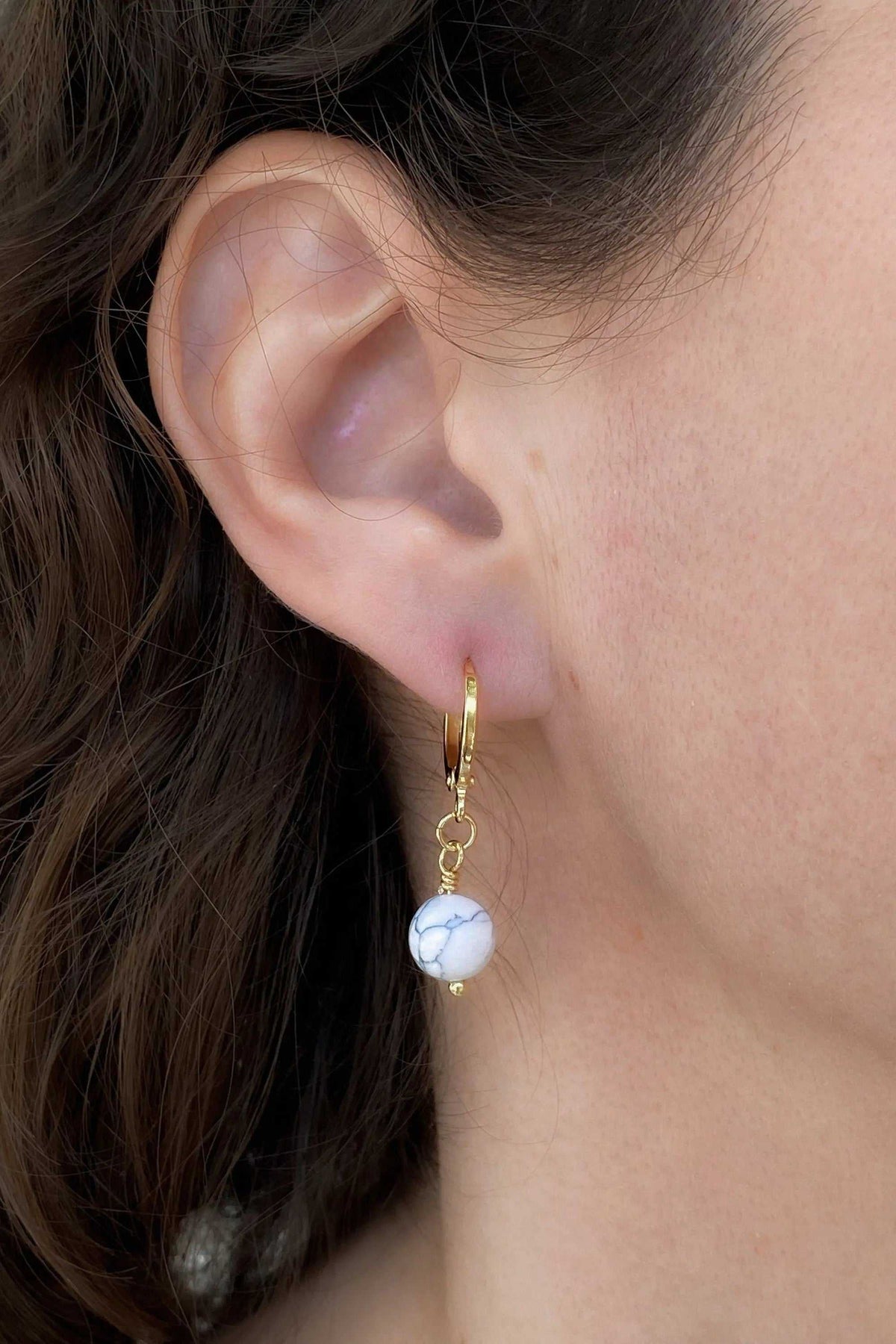 SABINA Gold Huggie Hoop Earrings in polished gold with a small white marbled bead charm dangling below each hoop