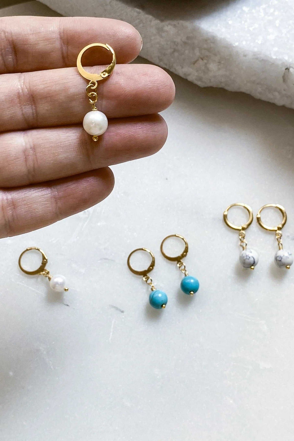 SABINA Gold Huggie Hoop Earrings in gold-tone metal with dangling white pearl-like beads and simple hoop closures