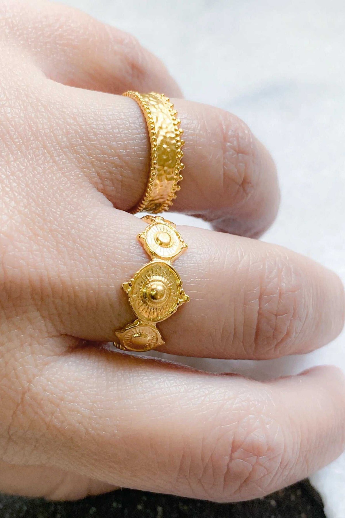 SHARMA Dotted gold ring in bright gold with raised dotted edges and ornate circular medallion details, shown on a finger