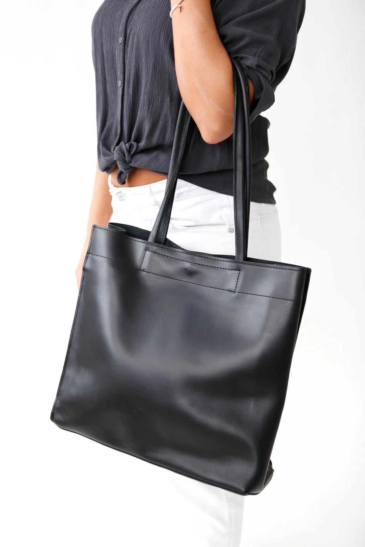 shoppers bag in black leather with long shoulder handles and a sleek minimalist tote design