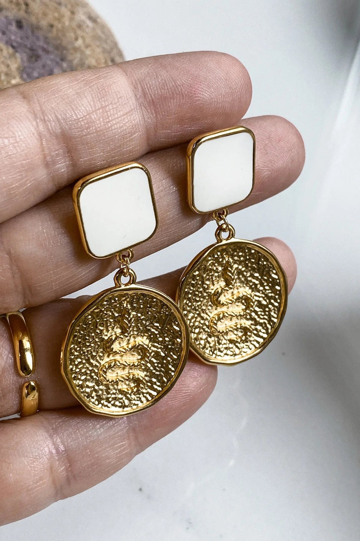 SNAKE Gold Coin Earrings with white square studs and textured round gold-tone coin drops featuring raised designs.