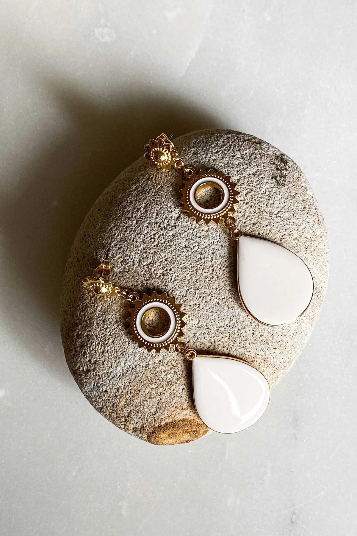 Statement Boho Earrings featuring gold-tone sunburst details, circular textured settings, and glossy white teardrop enamel drops