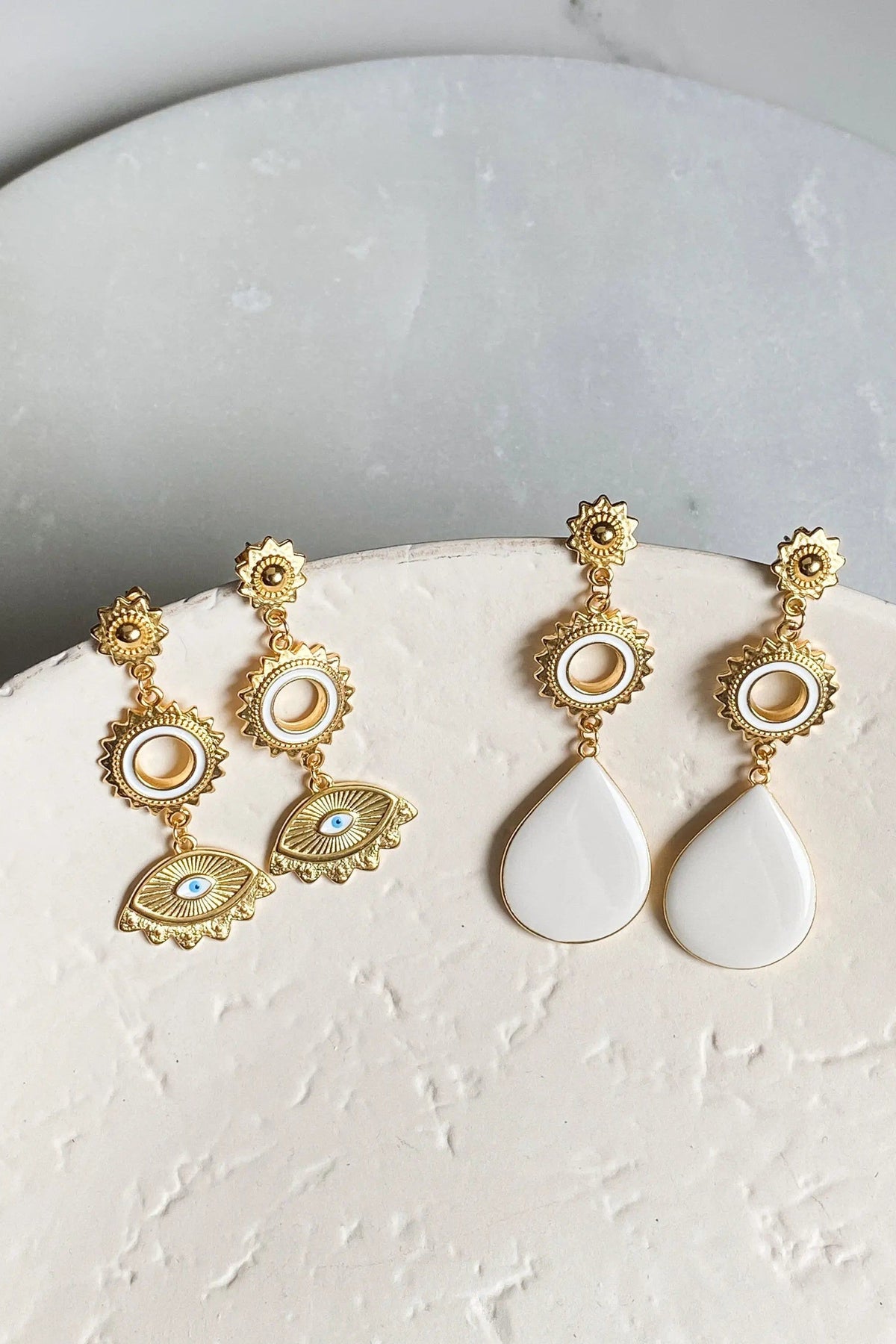 Statement evil eye earrings in gold-tone metal with ornate sunbursts, circular eye motifs, and white teardrop drops