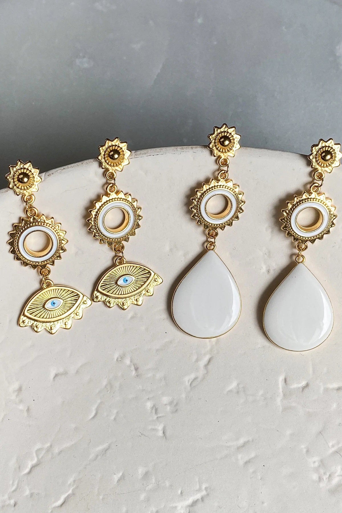 Statement evil eye earrings in gold-tone metal with sun and circular motifs, blue eye enamel and white teardrop stones