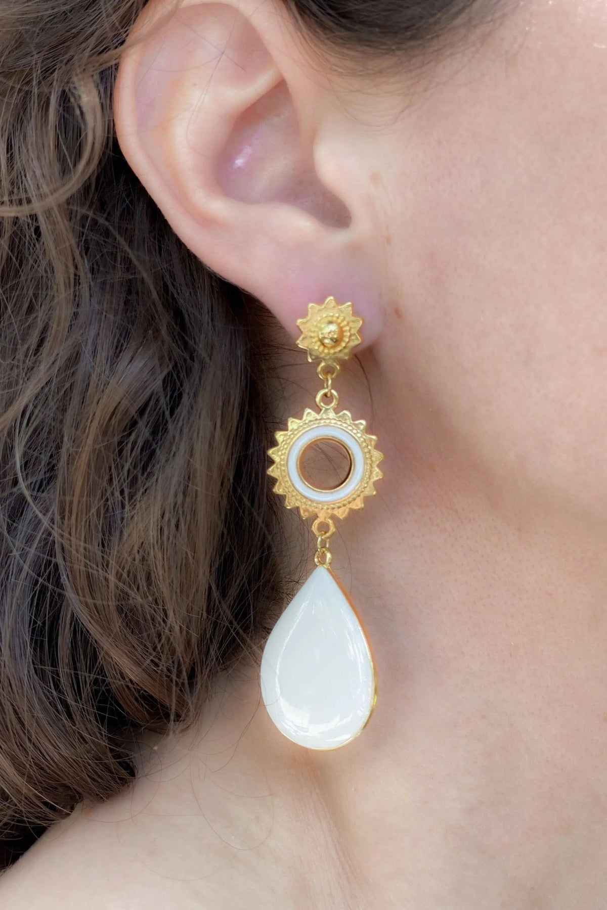 Statement evil eye earrings in gold-toned metal with ornate sunburst details, a circular eye motif and white teardrop pendant