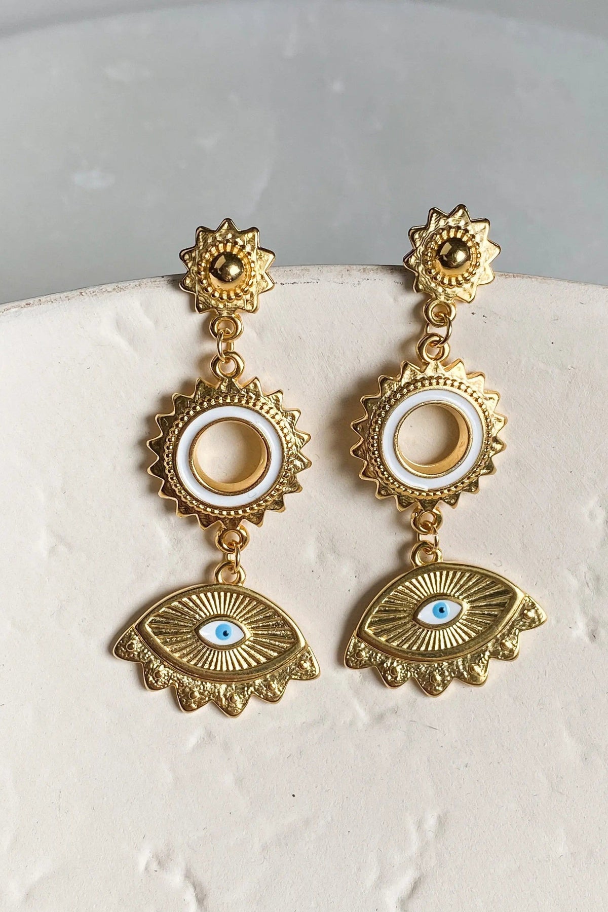 Statement evil eye earrings in textured gold-tone metal with dangling circular frames and blue enamel eye motifs