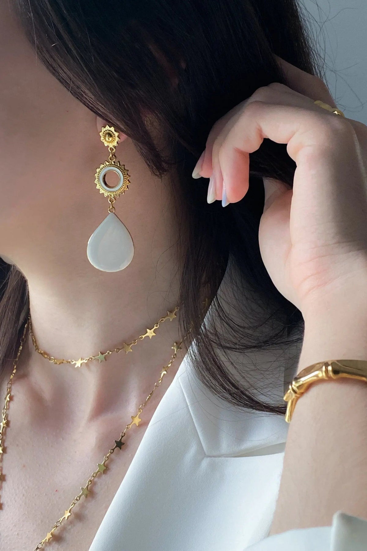 Sun drop earrings with gold-tone sunburst settings, a pale blue teardrop stone, and a small circular accent