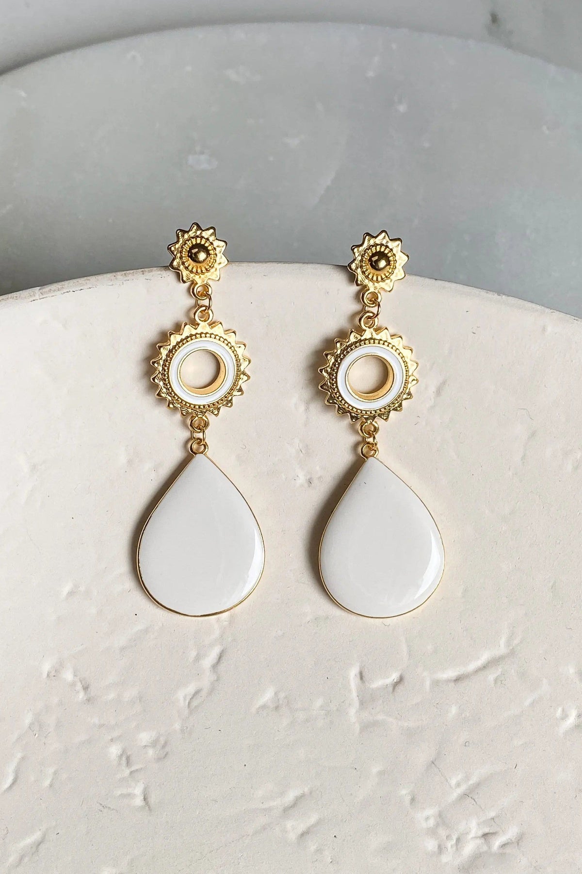 Sun drop earrings in gold-tone metal with ornate sunburst studs, circular white accents and smooth teardrop pendants