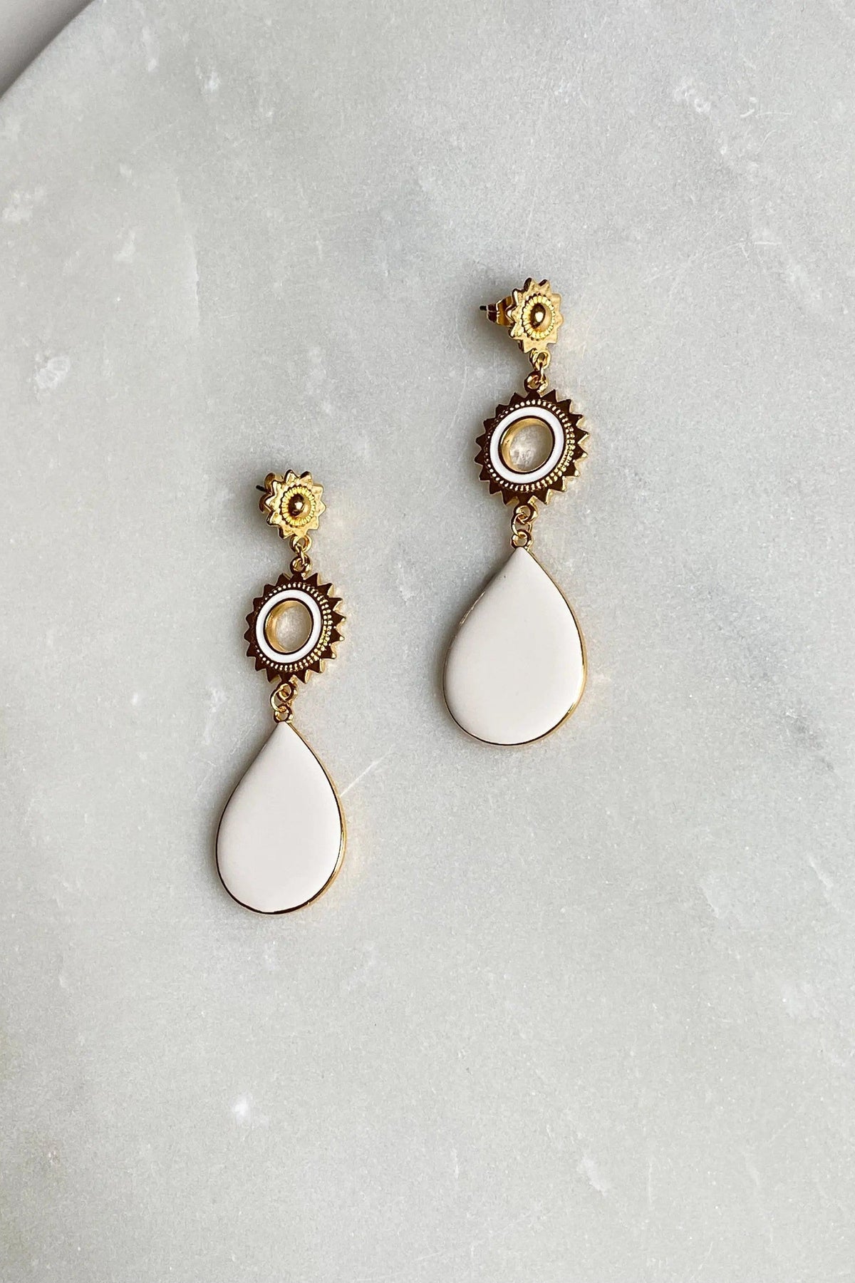 Sun drop earrings in gold-tone metal with ornate sunburst details, round pearl-like centers, and smooth white teardrop drops