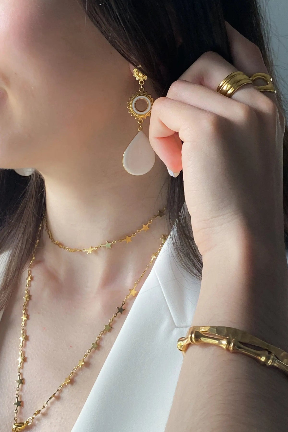 Sun drop earrings in gold-tone metal with a circular sunburst detail and a smooth white teardrop pendant