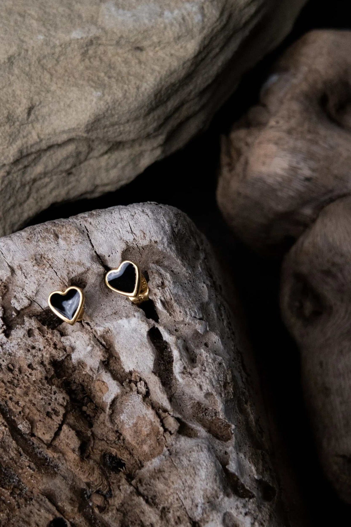 Tiny black heart earrings in gold-toned metal with glossy black heart centers and titanium pins
