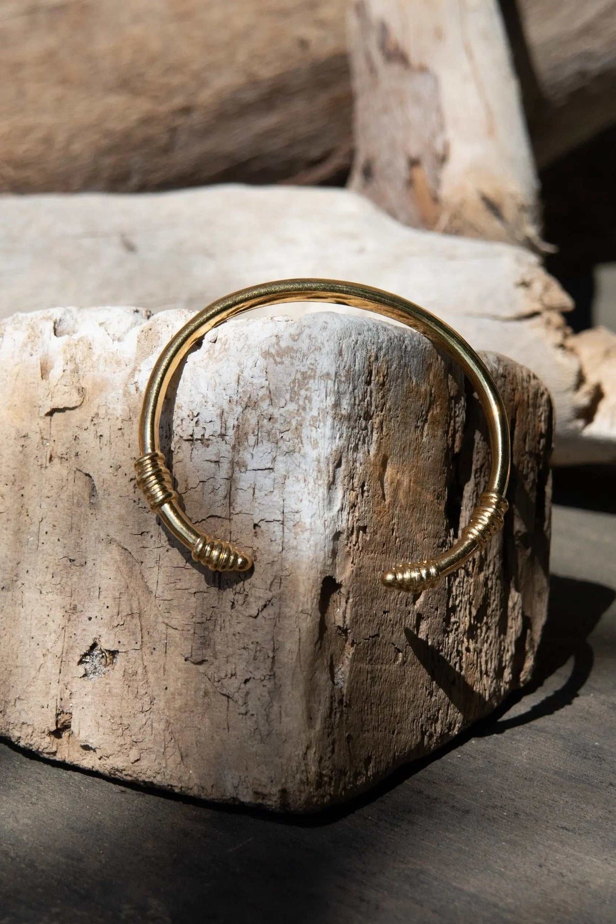 Tribal slim Bracelet in polished gold-tone metal, featuring a narrow open cuff with coiled tribal-style end details